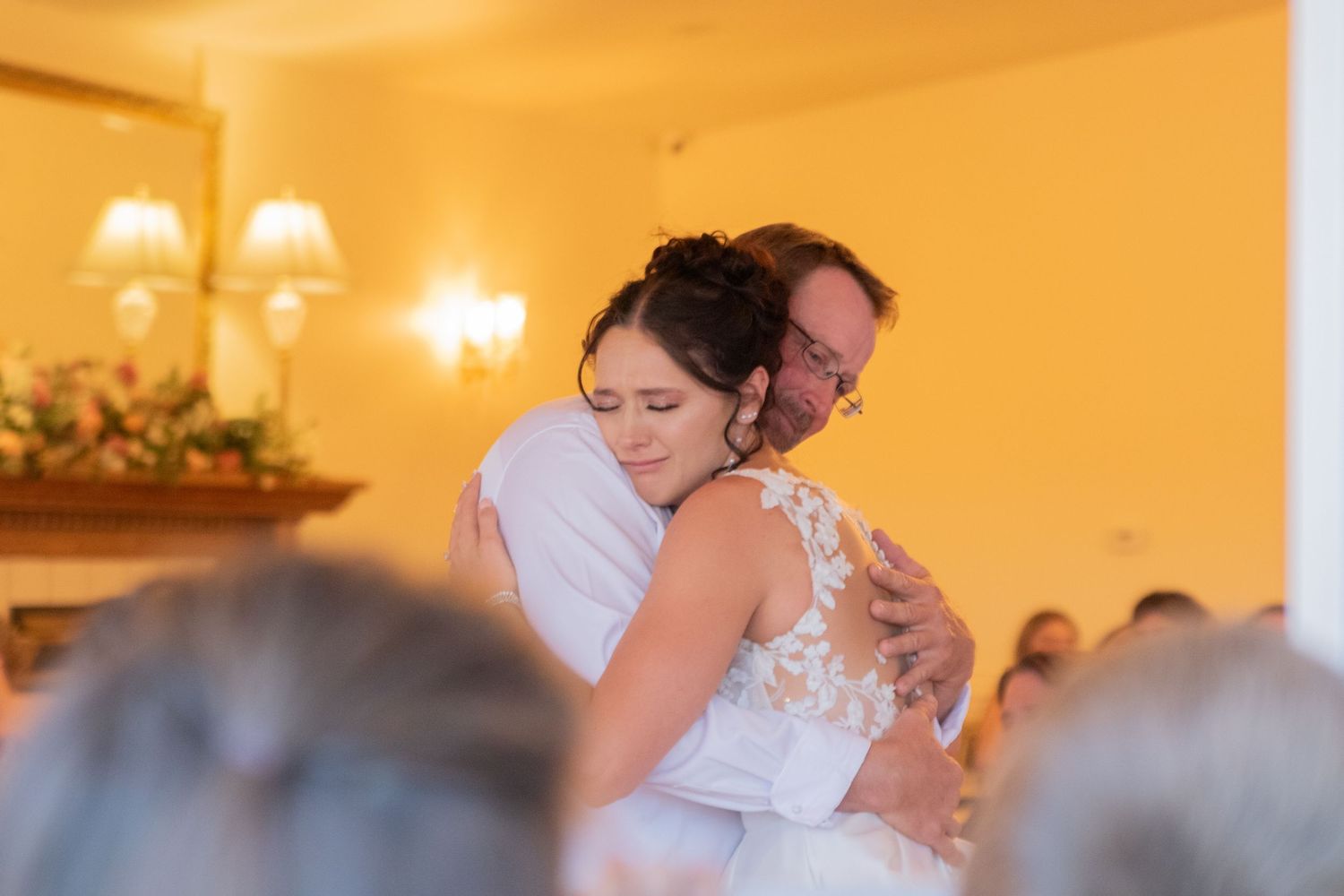 Wedding celebration guests dancing and embracing in a golden-lit reception room.