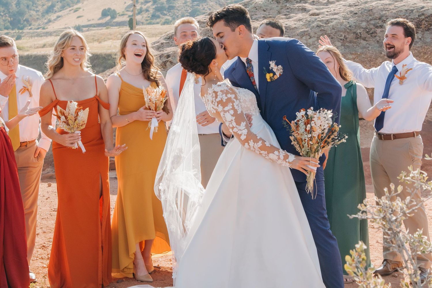 Wedding party in colorful attire posing against mountainous backdrop.