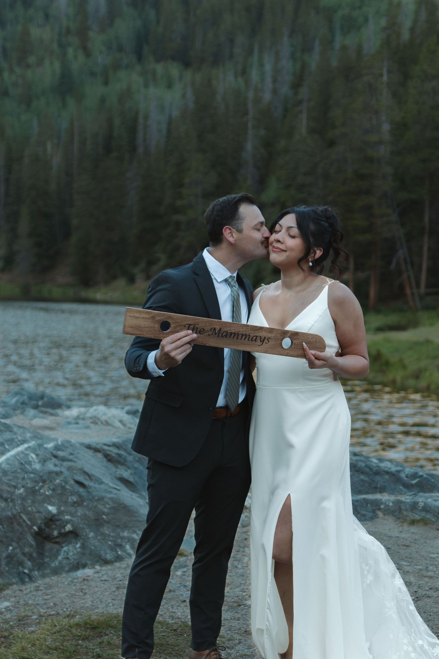 A romantic wedding moment near a scenic mountain lake with the couple playfully interacting.