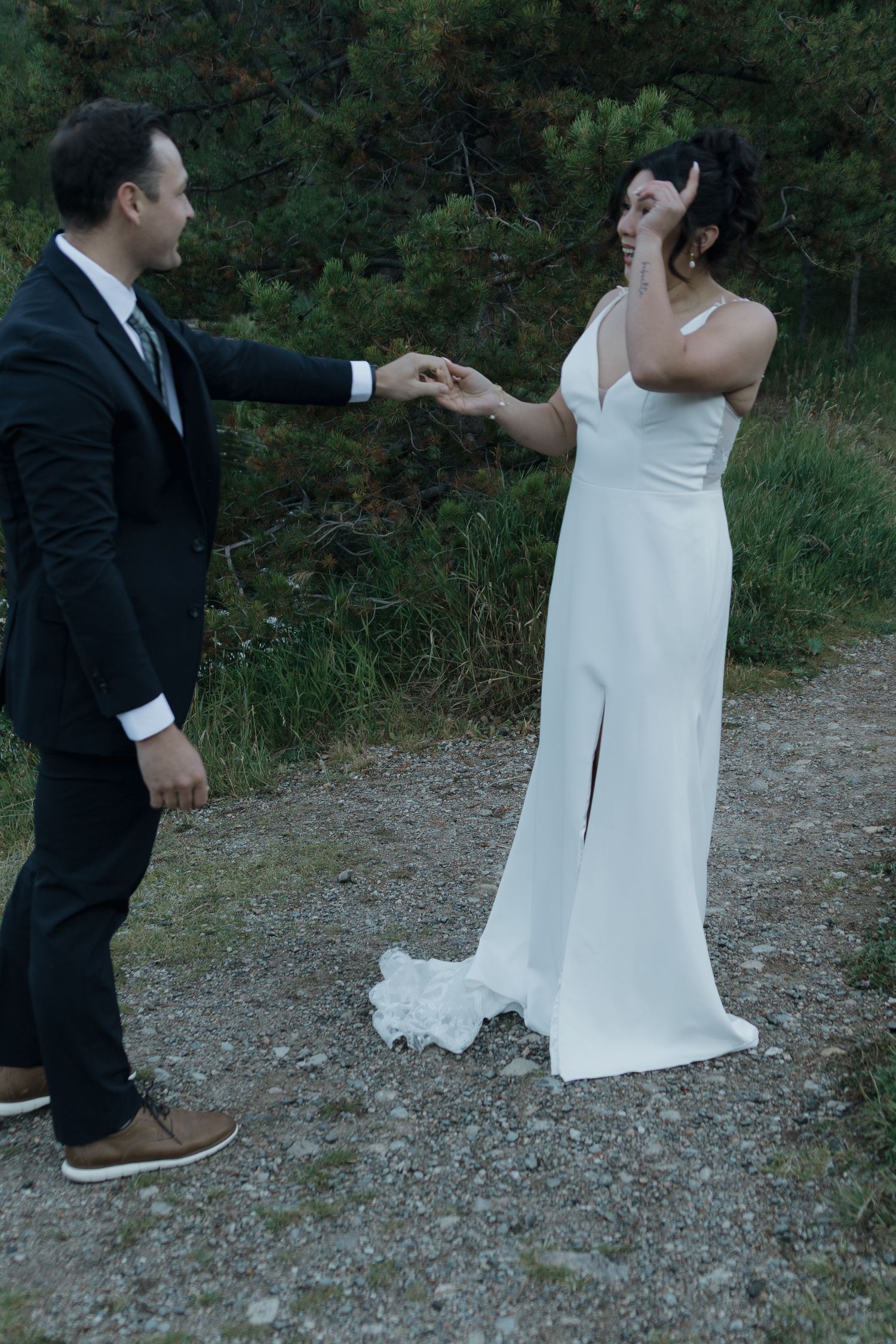 A couple in wedding attire shares candid moments on a gravel path surrounded by nature.