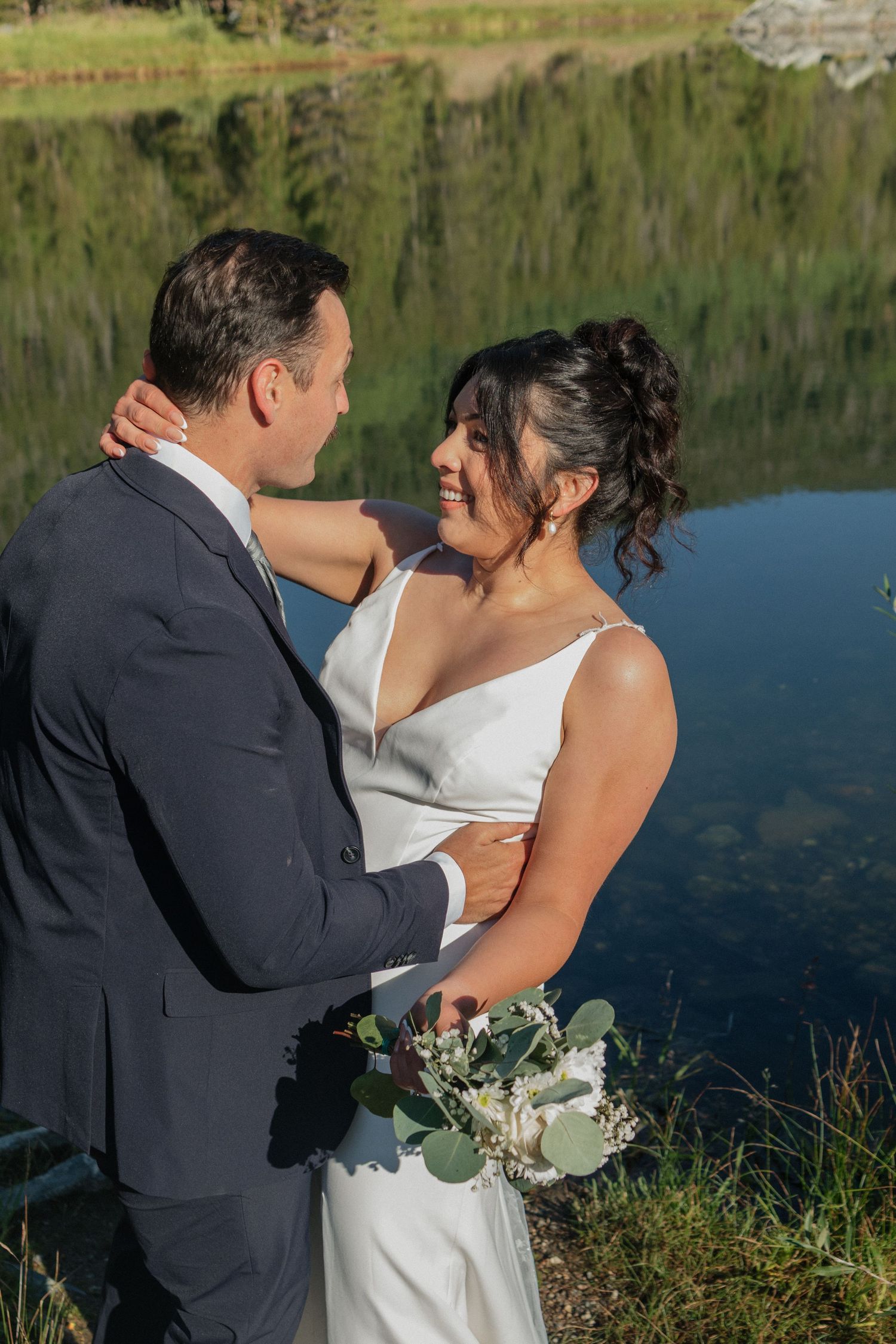 An intimate wedding moment captured by a scenic lake with mountains and forest in the background.