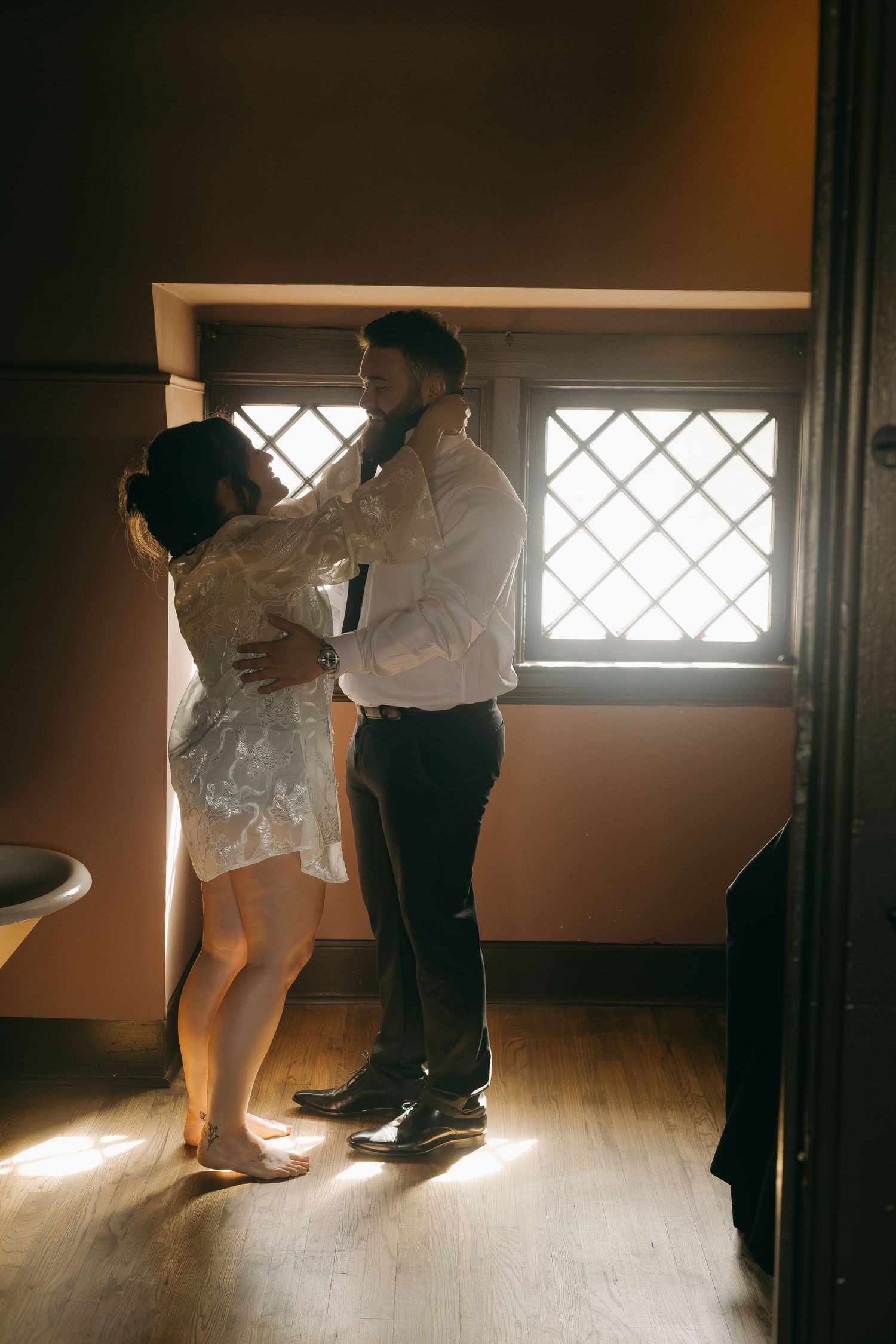 Two people dancing in dramatic window light on a wooden floor.