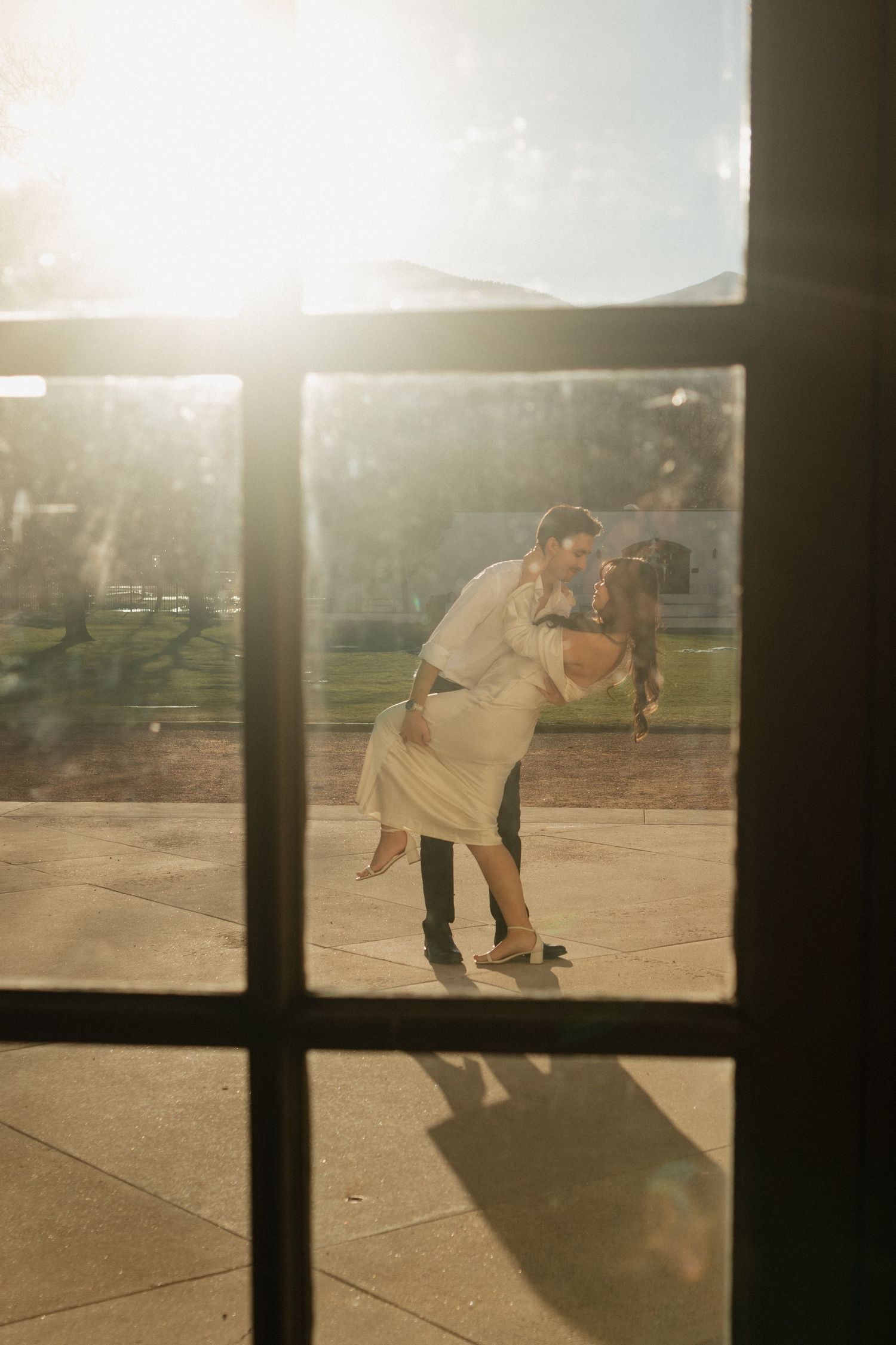 A silhouetted couple dancing in golden sunlight through window frames.