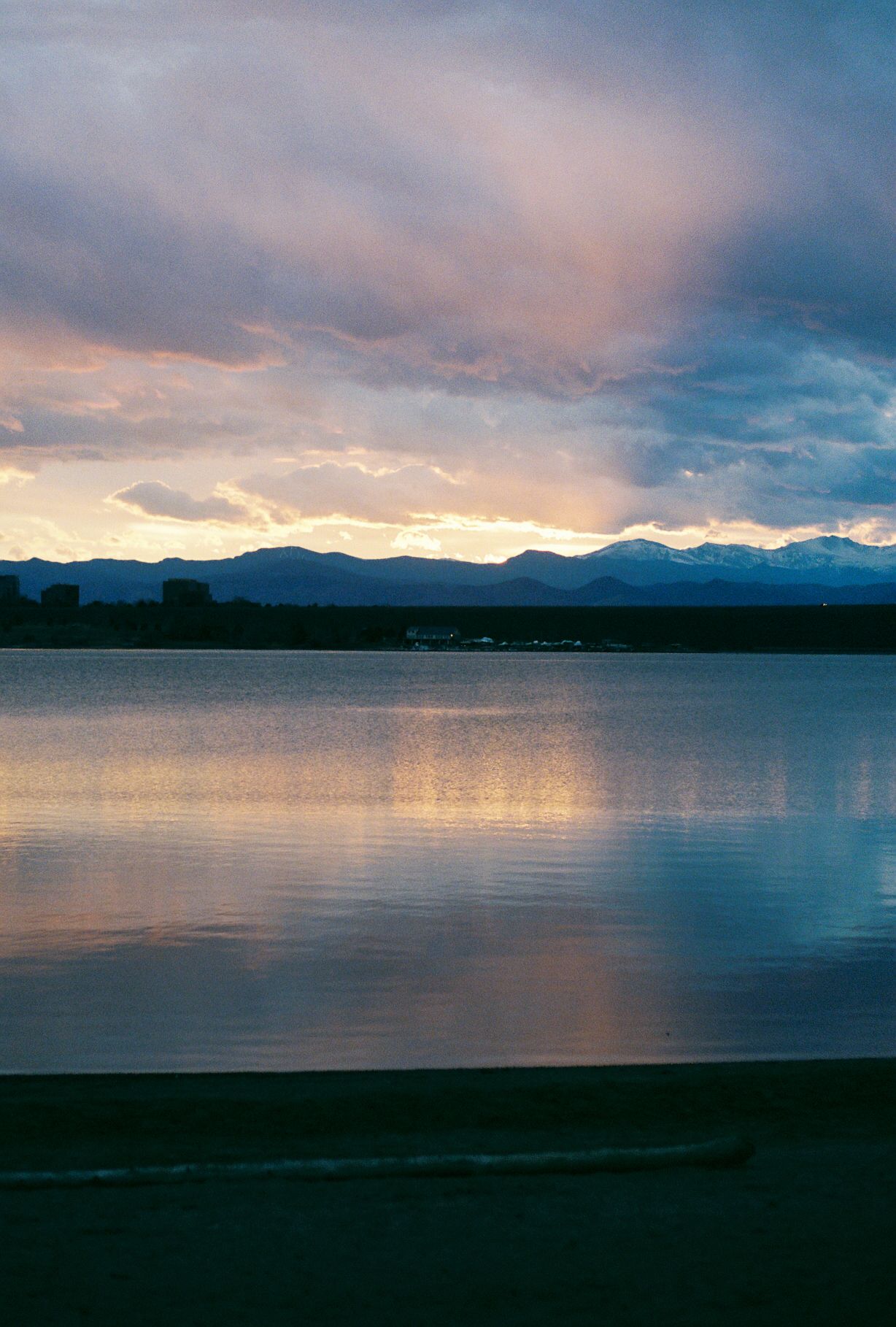 A serene lake landscape at sunset with mountains silhouetted in the background.