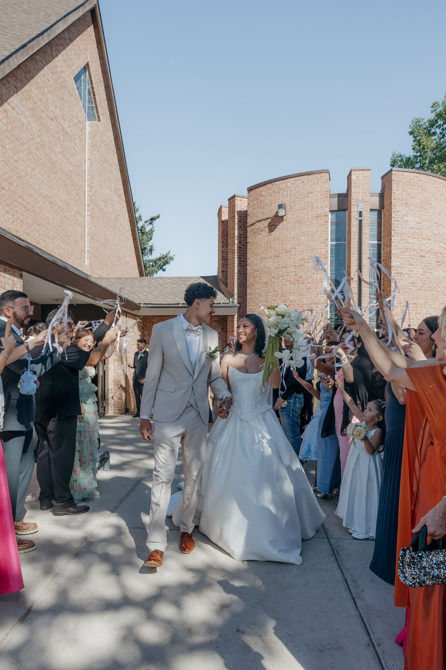 Newlyweds exit church as guests wave ribbon wands in joyful wedding sendoff celebration.