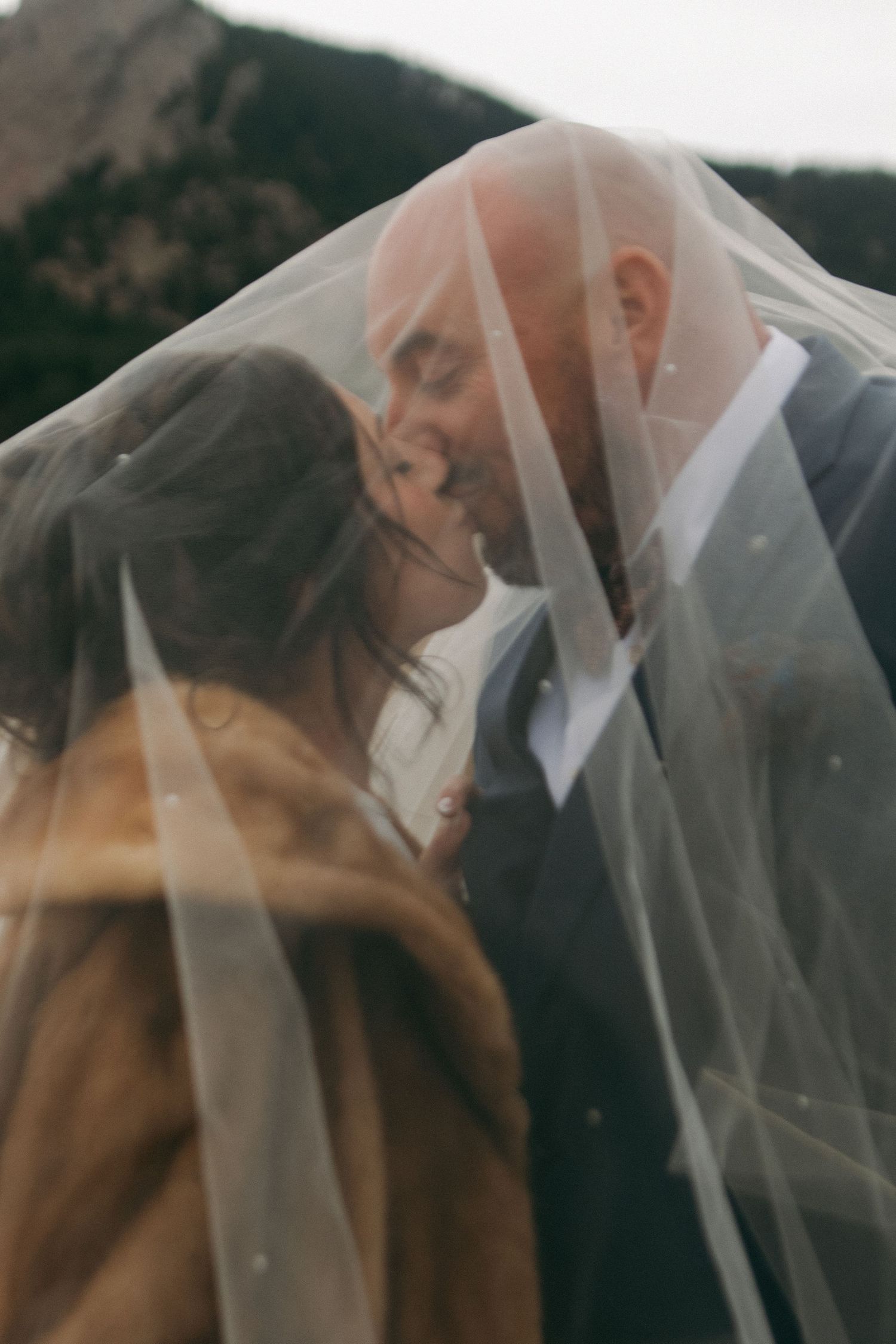 A romantic wedding moment captured through a delicate white veil in soft focus.