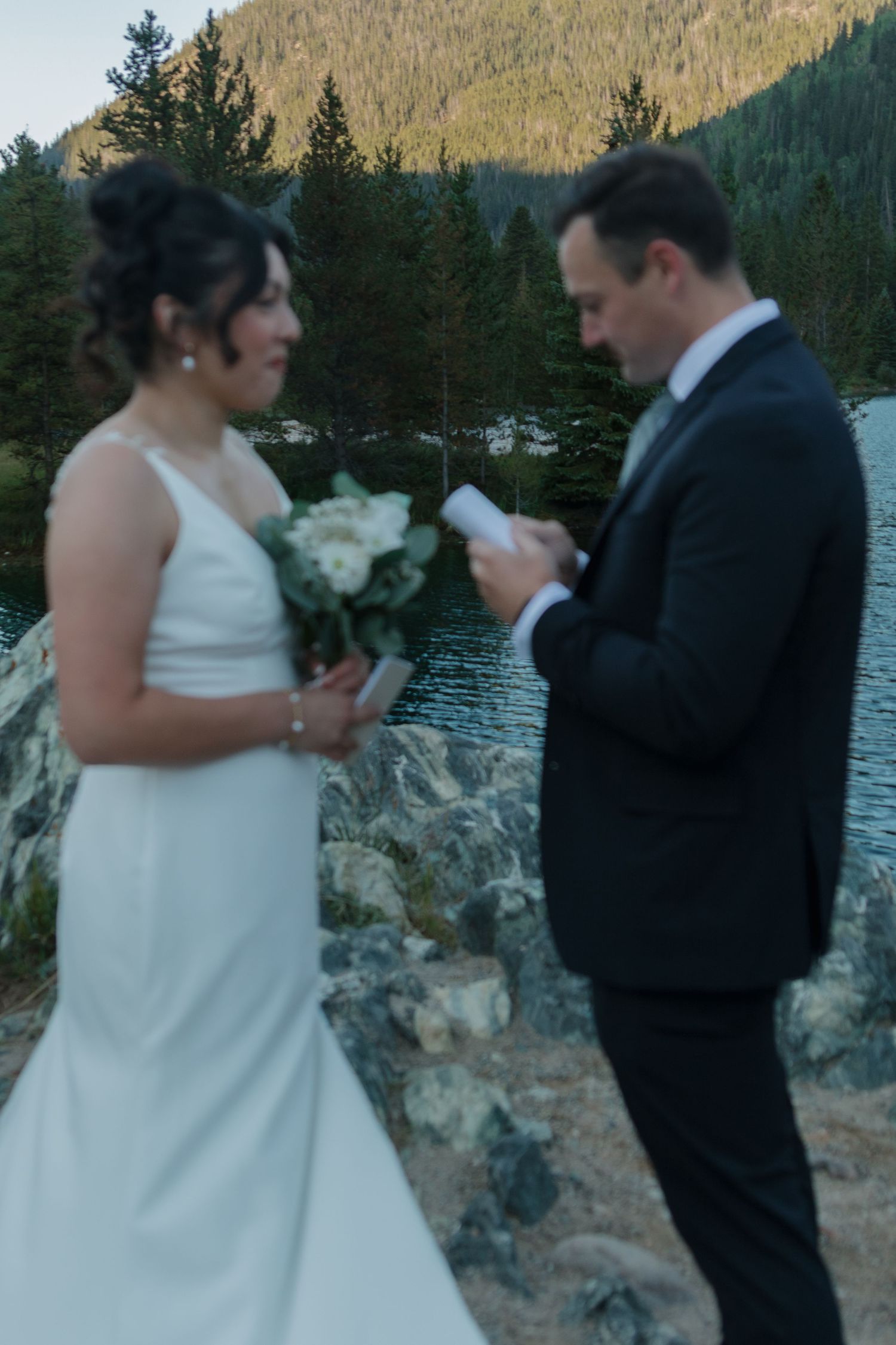 Couple exchanging wedding vows on a rocky overlook with mountain scenery in the background.