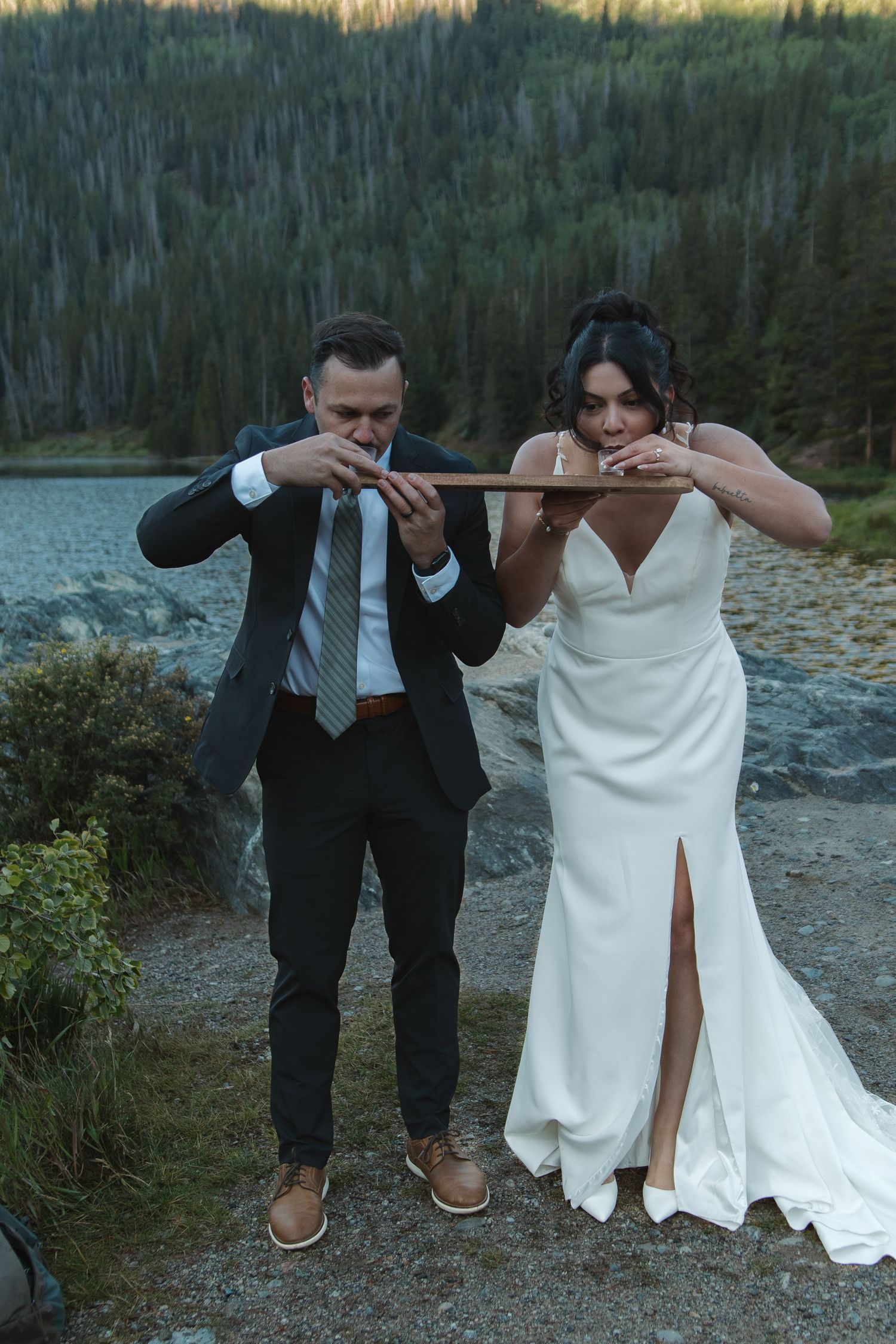 Playful wedding couple pretending to play violin by mountain lake.