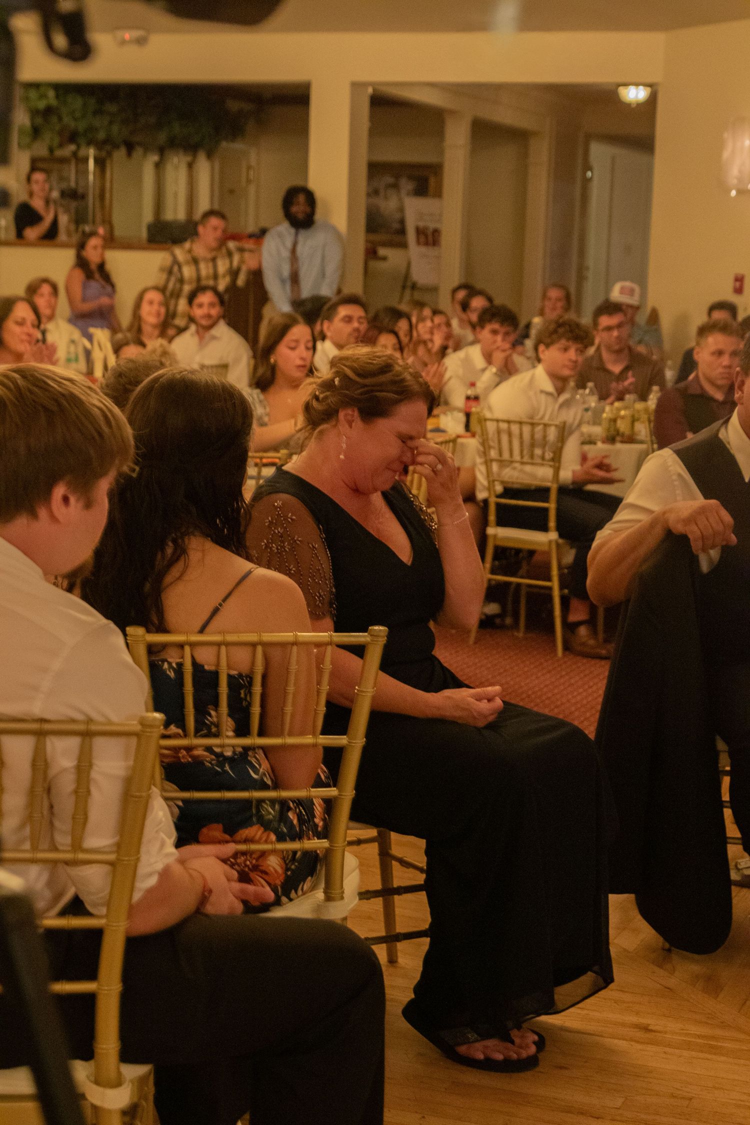 Wedding reception guests seated at round tables in a warmly lit ballroom.