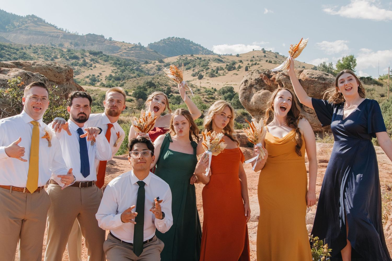 Wedding guests and party members pose joyfully with mountain scenery behind them.