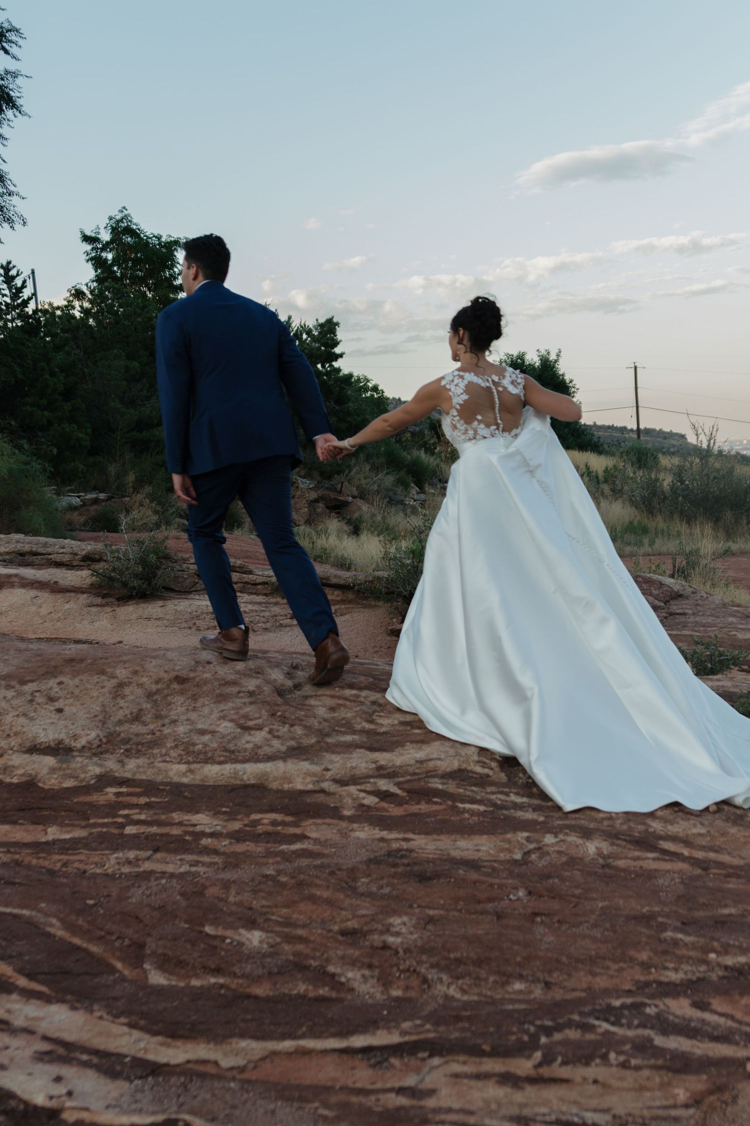 Couple walking together on red rock formations during sunset wedding photoshoot.