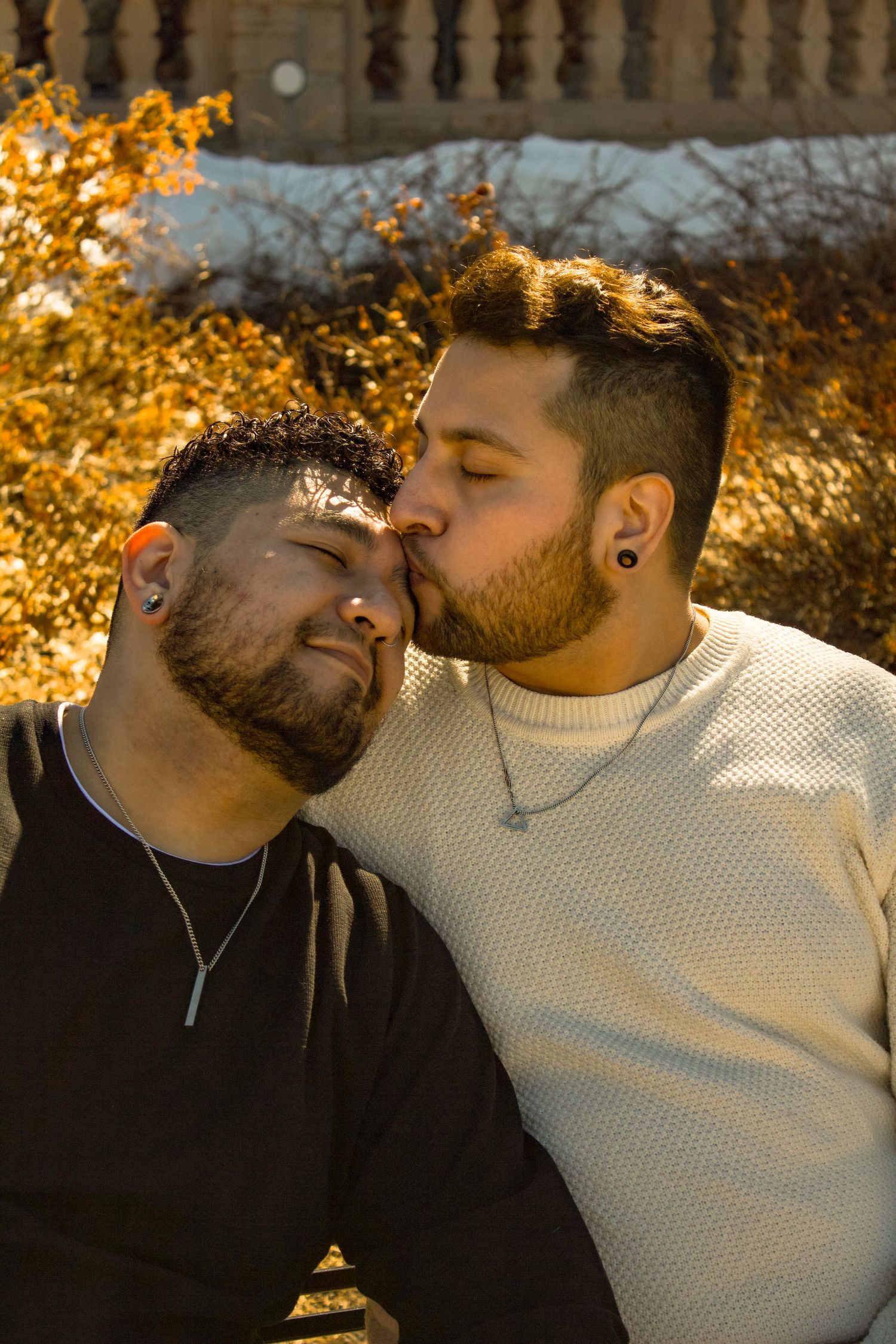 A gentle moment between two people backdropped by golden autumn bushes and stone architecture.