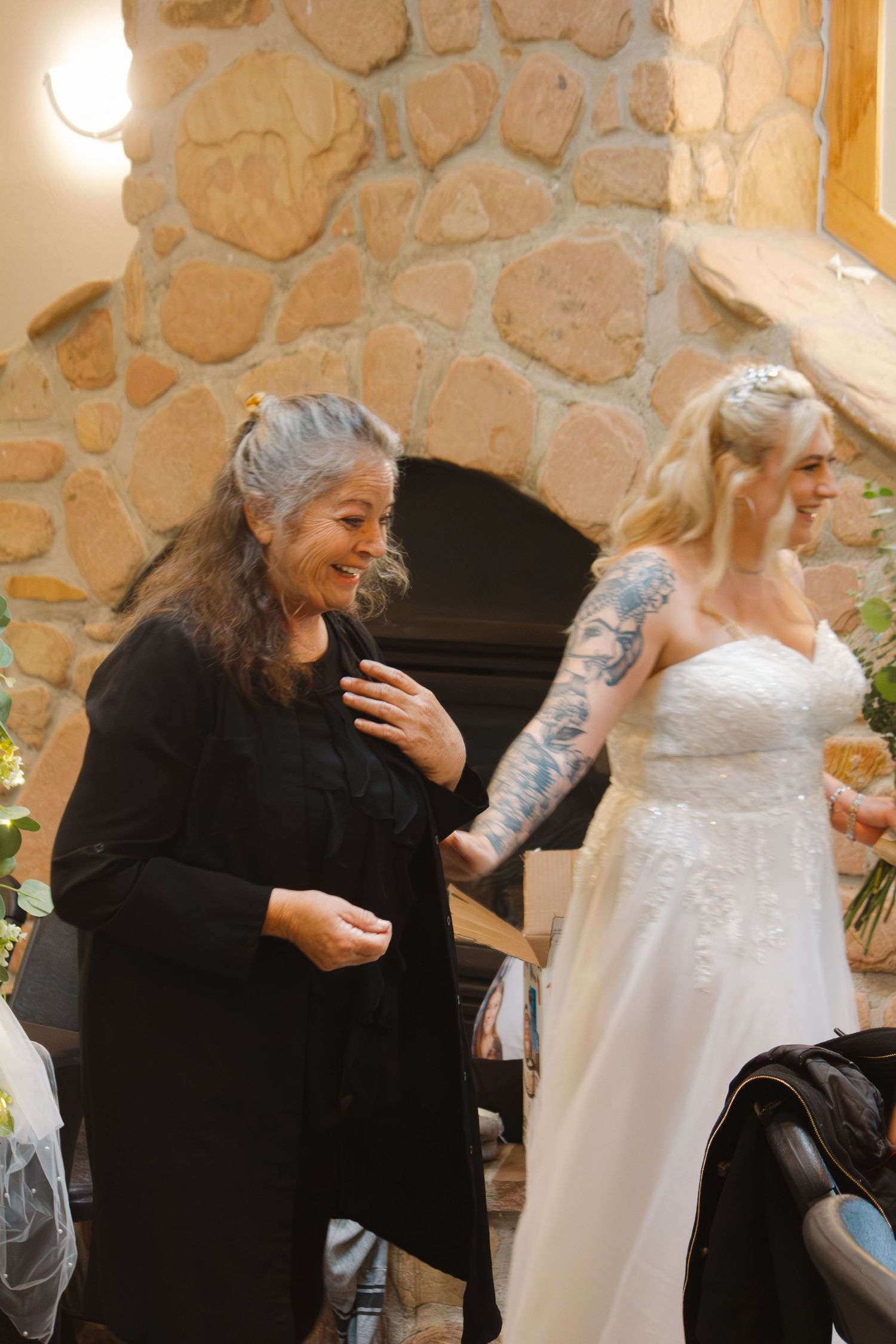 A joyful wedding moment near a stone fireplace showing a bride and officiant sharing laughter.