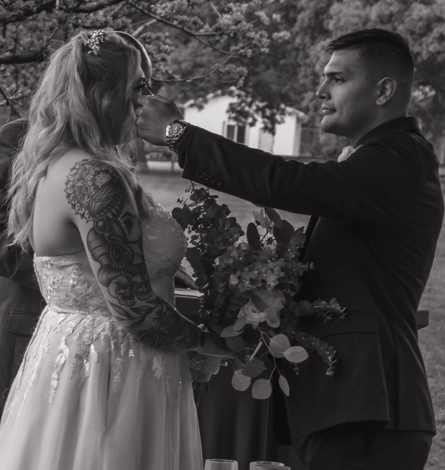 A black and white photo captures an intimate moment between newlyweds holding a floral bouquet.
