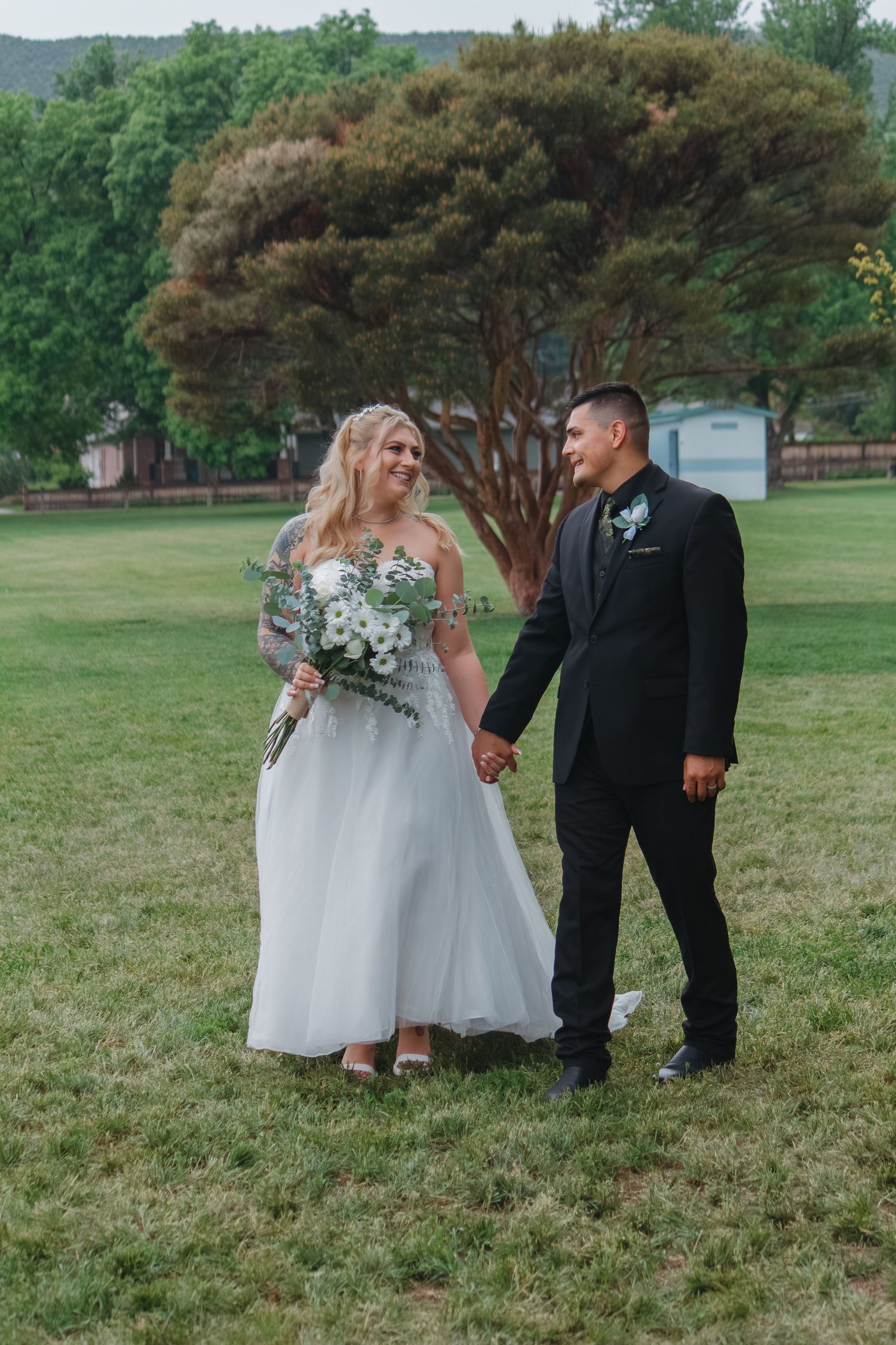 Wedding party stands on grassy lawn near trees during outdoor ceremony.