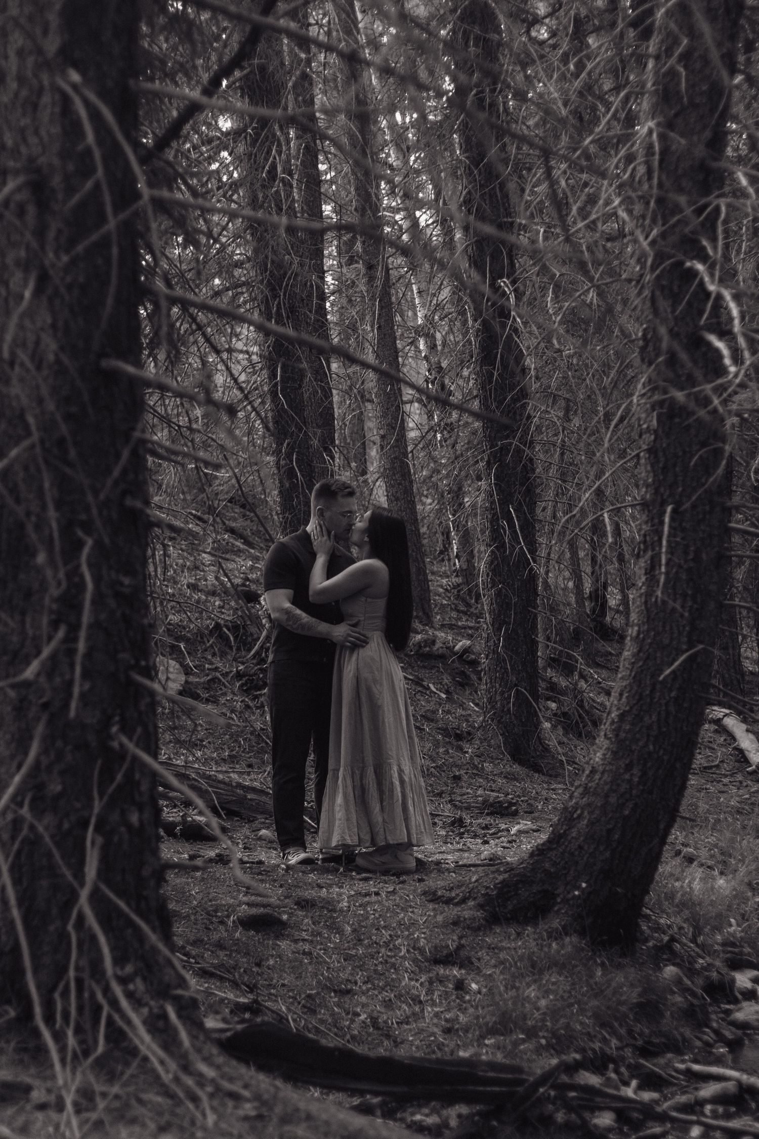 Black and white photo of a couple's silhouette in a moody forest setting.