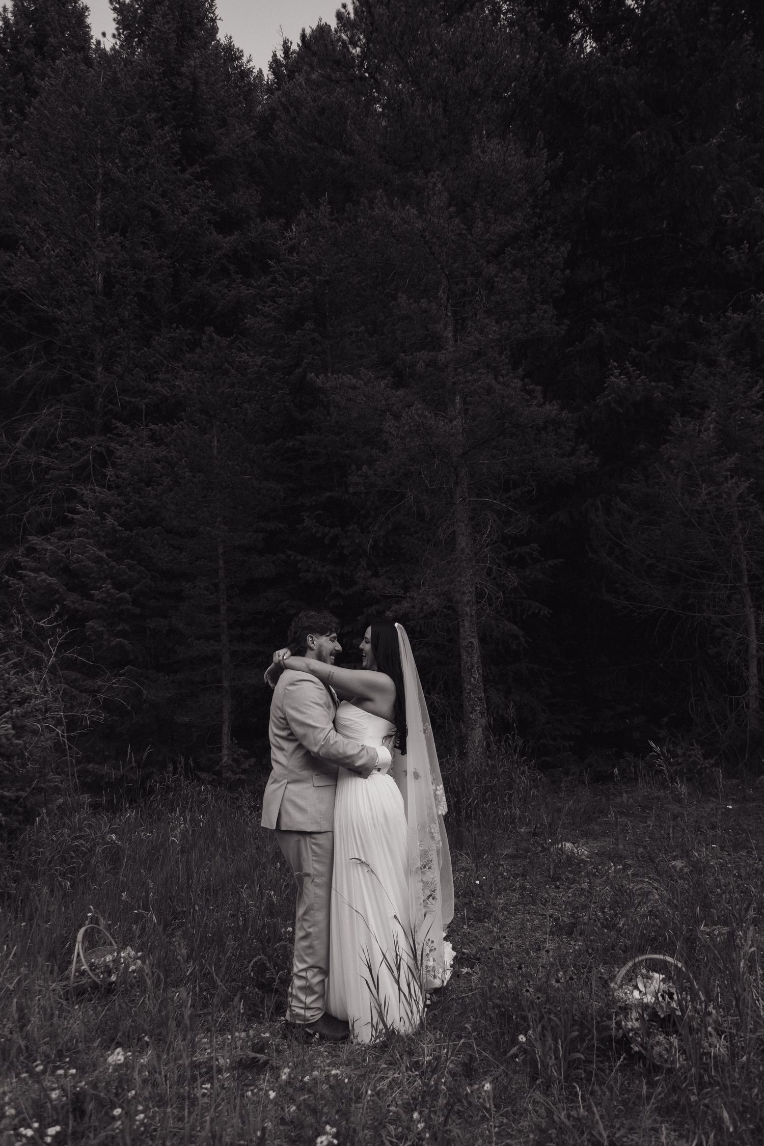 Black and white photo of bride and groom kissing in a forest meadow.