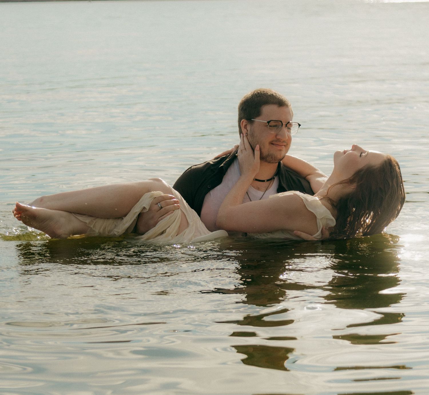 Couple sharing a romantic moment in a lake, woman reclined in mans arms over calm water.