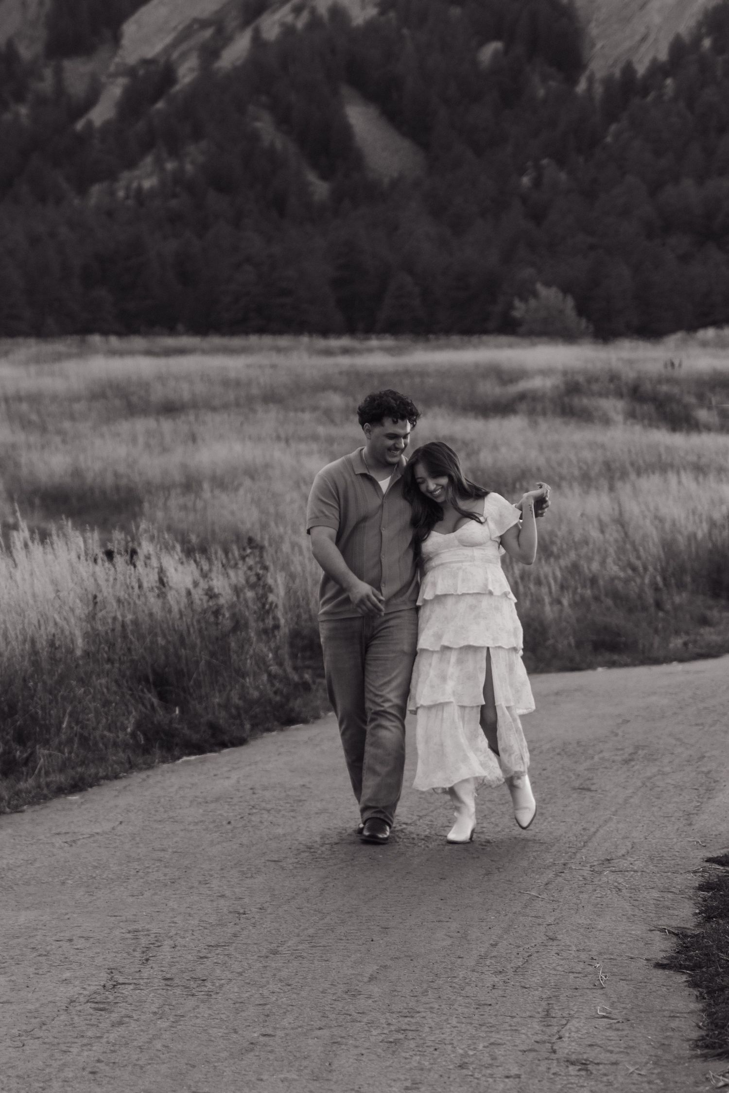 Black and white photo of couple walking closely together on rural path through meadow.