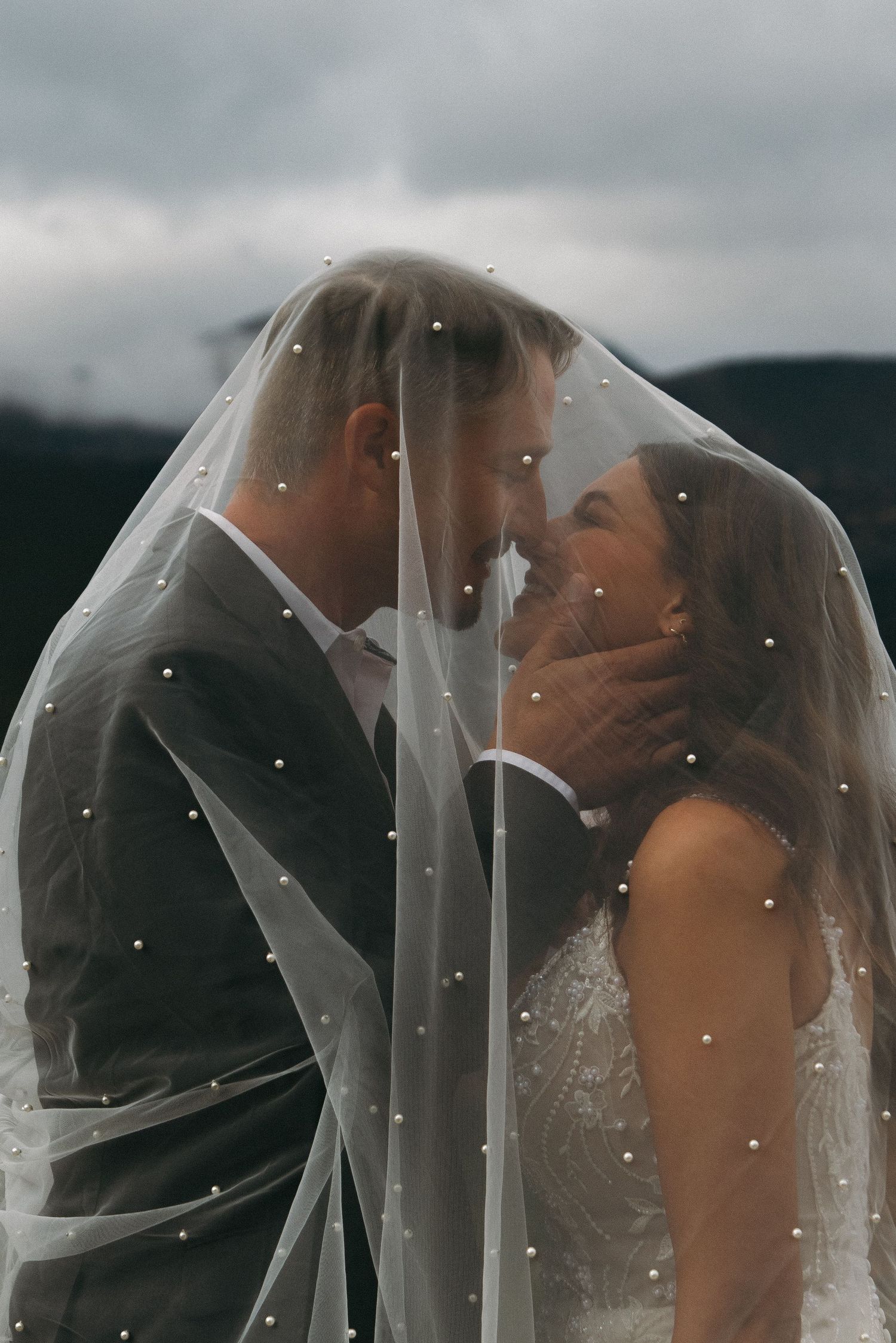 A romantic wedding sequence shows a couple kissing under a delicate white veil against a moody sky background.