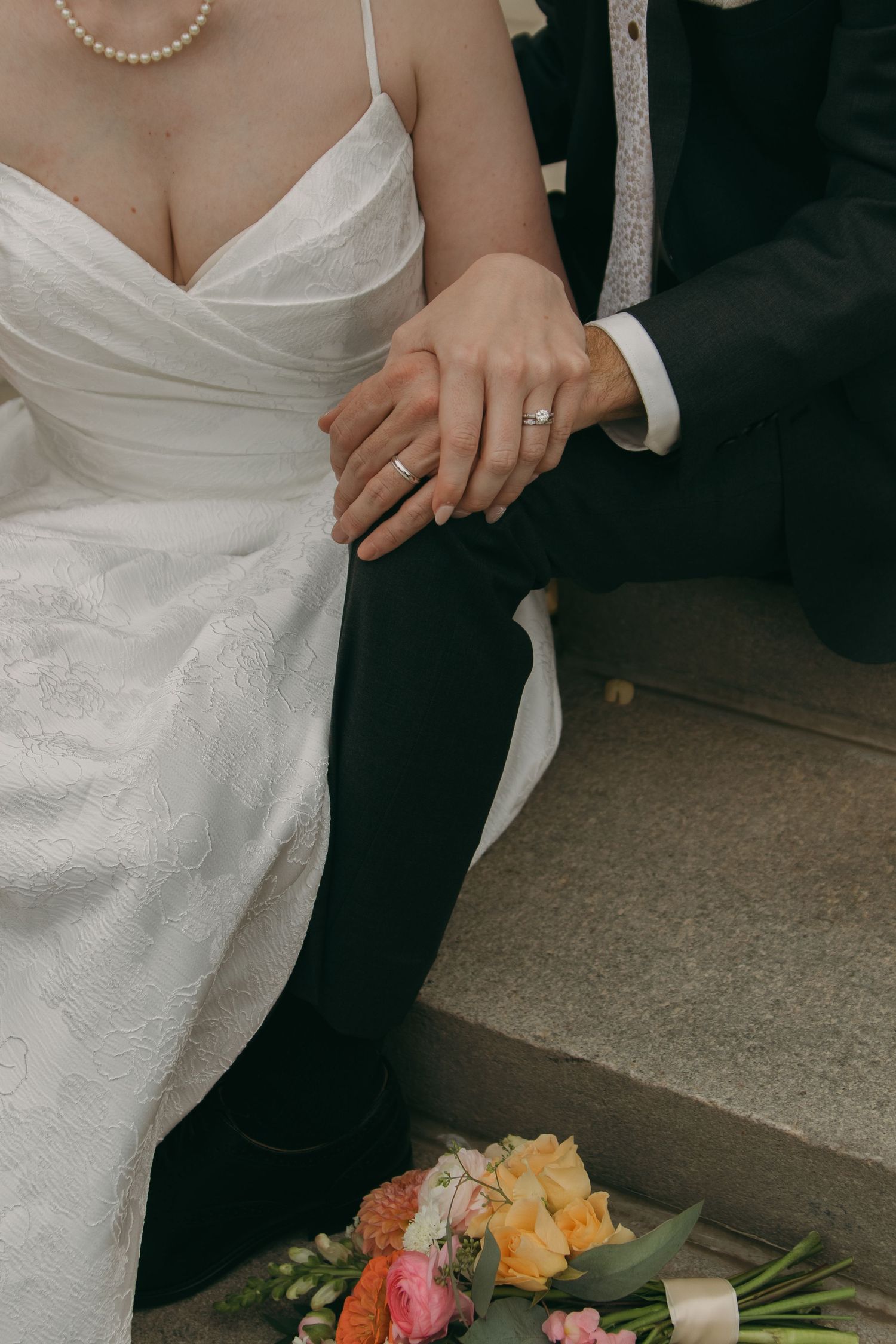 Cropped view of newlyweds in formal wedding attire with a colorful floral bouquet visible in the corner.