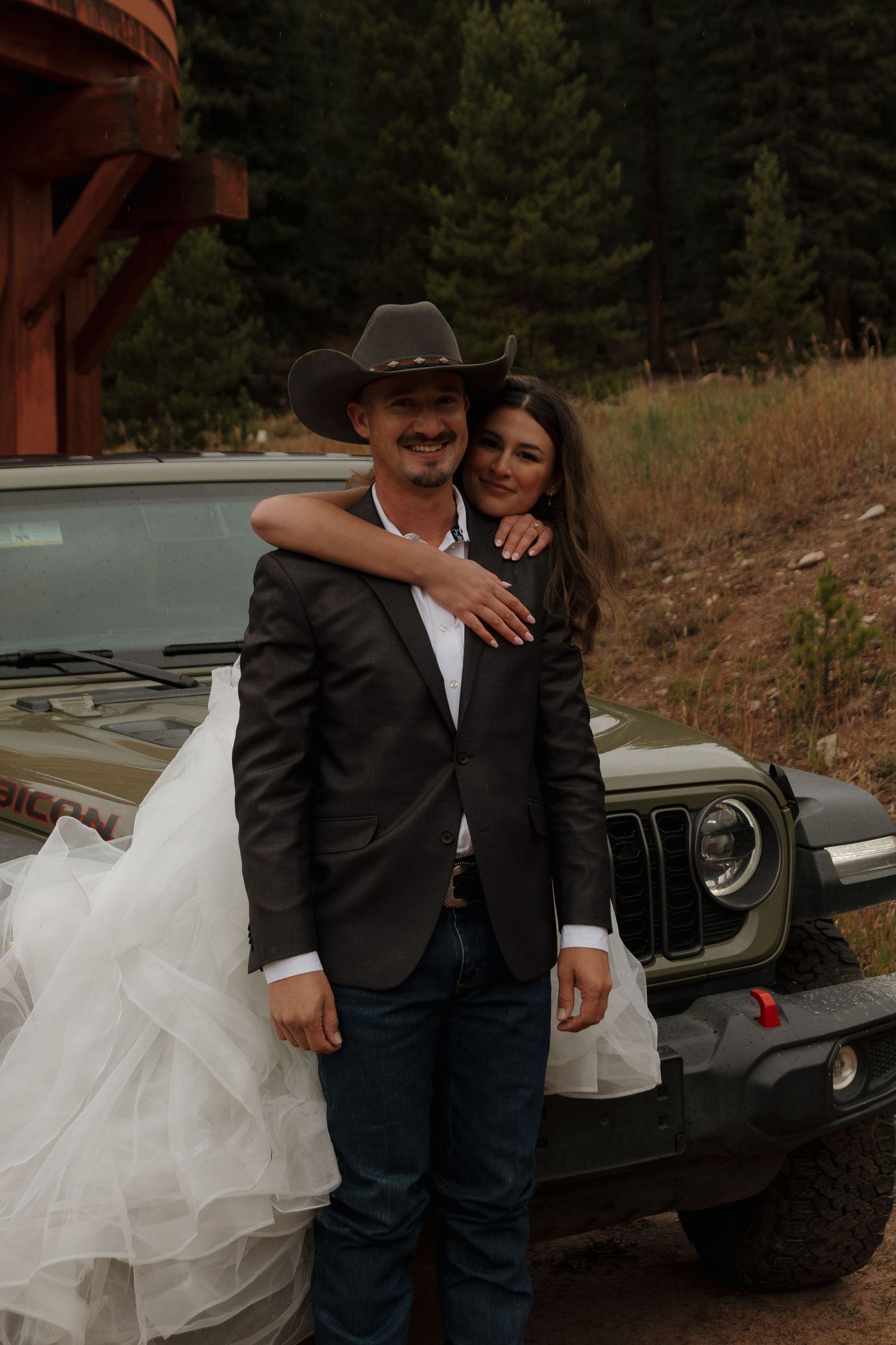 A couple poses together in front of a Jeep during their rustic mountain wedding.