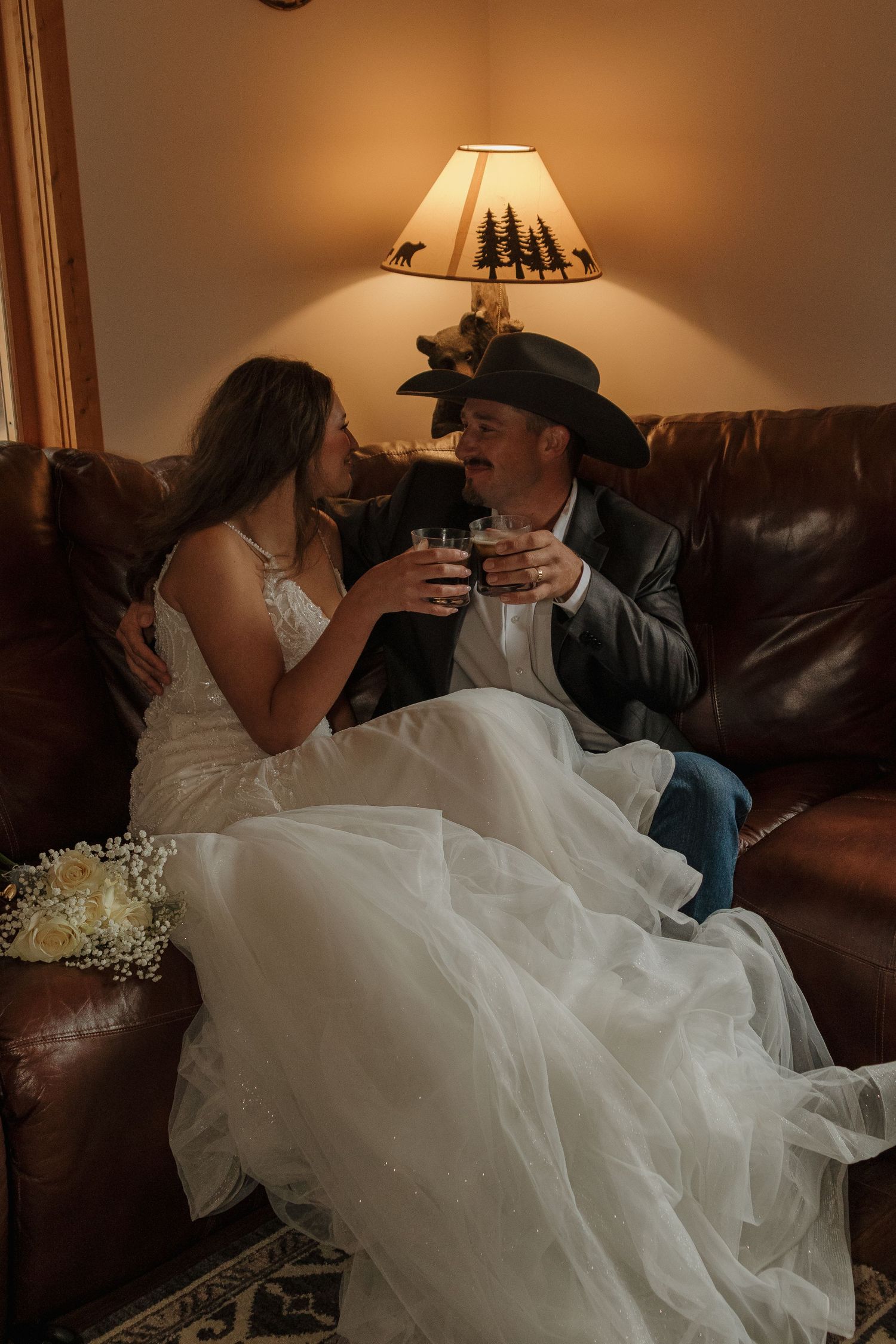 A romantic moment on a brown leather couch with soft lamp lighting in a cozy living room.