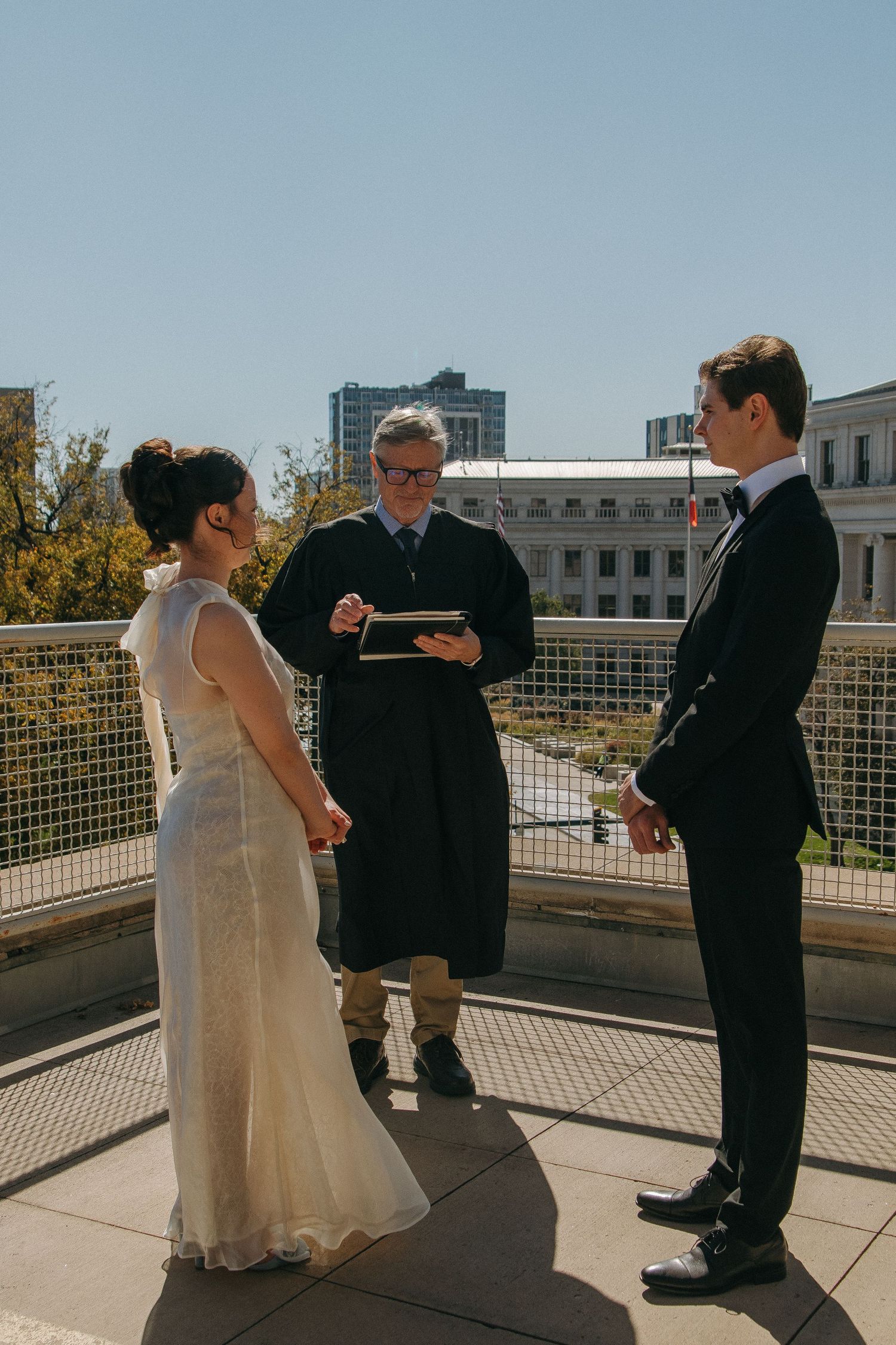 A wedding ceremony taking place on a sunny rooftop terrace with city buildings in the background.