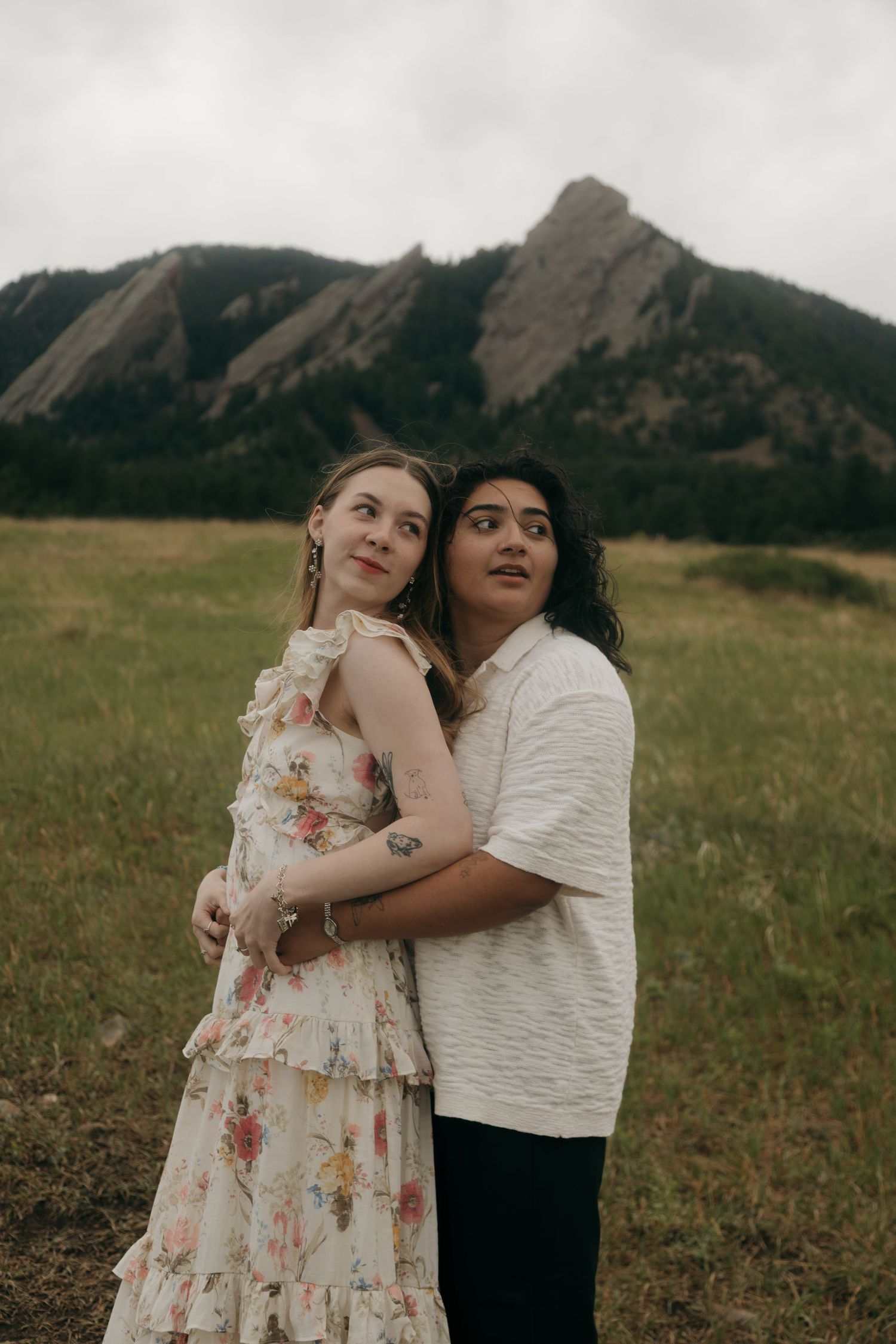 Couple embracing in a meadow with the Flatirons of Boulder, Colorado in the background on a cloudy day.