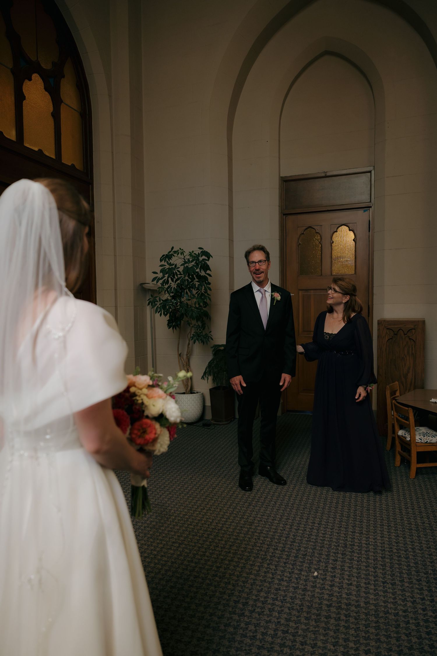 Groom smiles at bride during first look moment in church hallway.