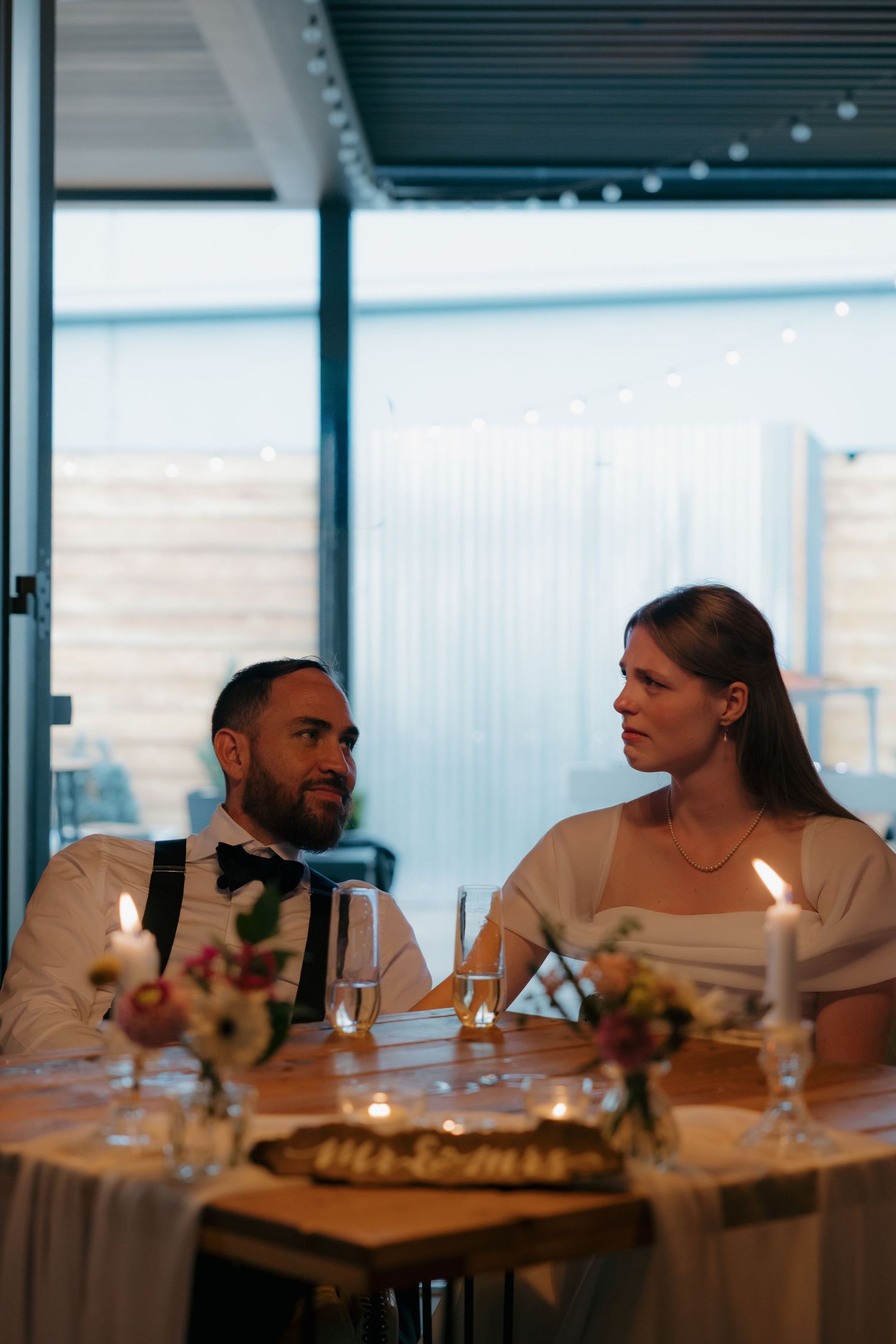 Couple sharing an intimate moment at a candlelit wedding reception table with floral centerpieces and city views.