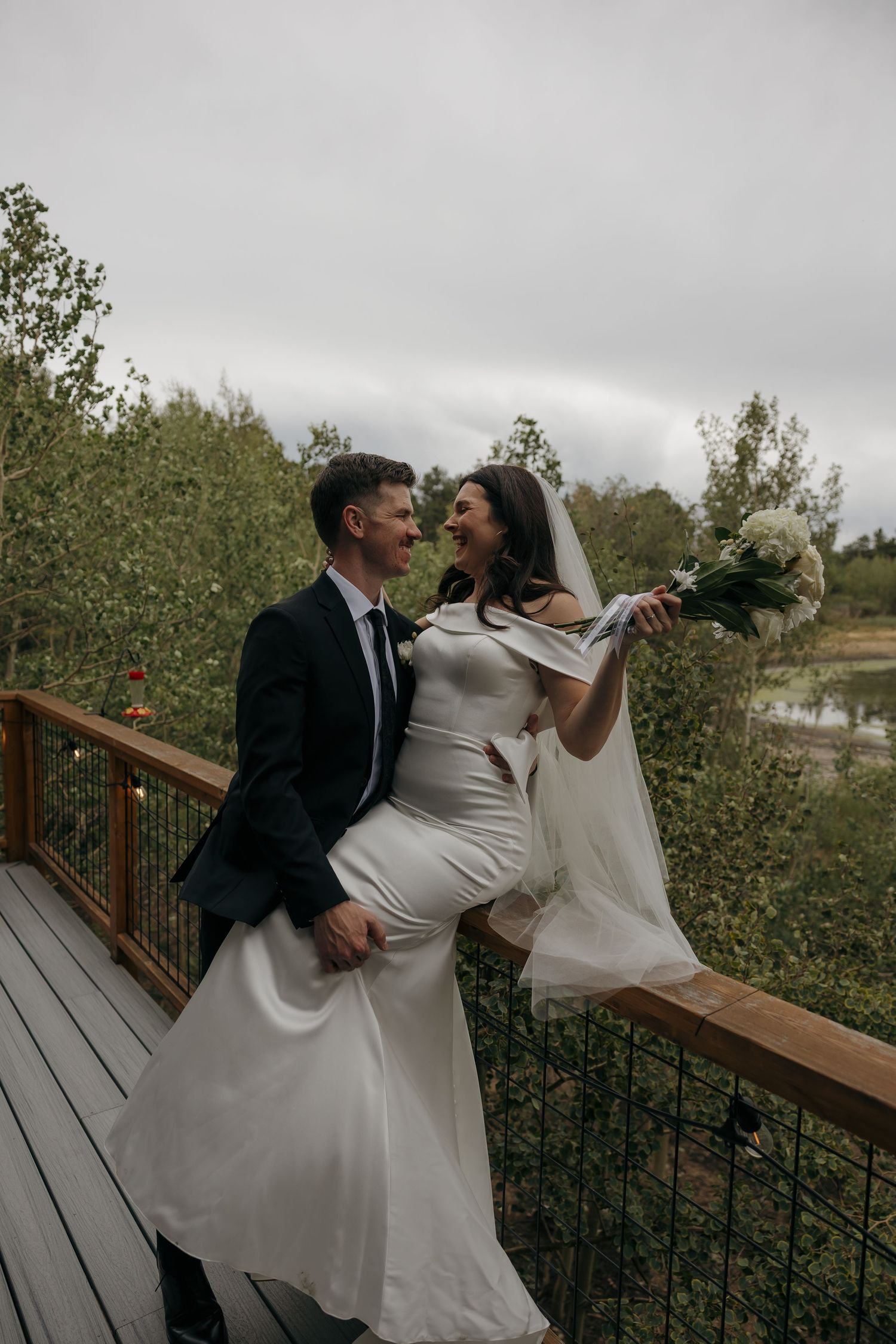Happy bride and groom sharing a romantic moment on a wooden deck surrounded by lush greenery.