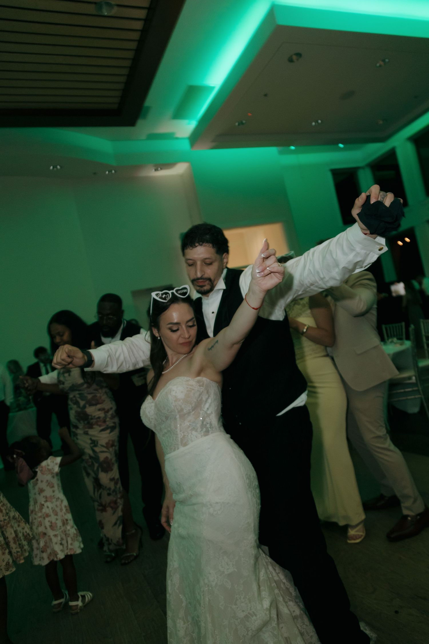 Bride and groom dancing together at wedding reception under green ambient lighting.