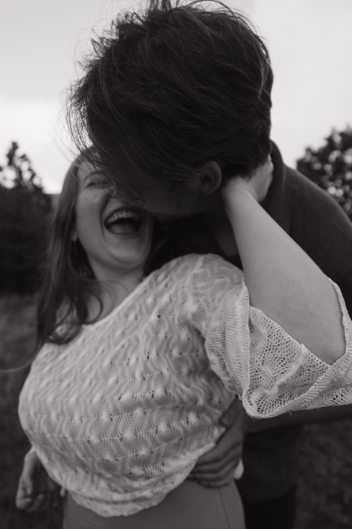 A woman laughs joyfully as her partner kisses her cheek in a black and white photo.