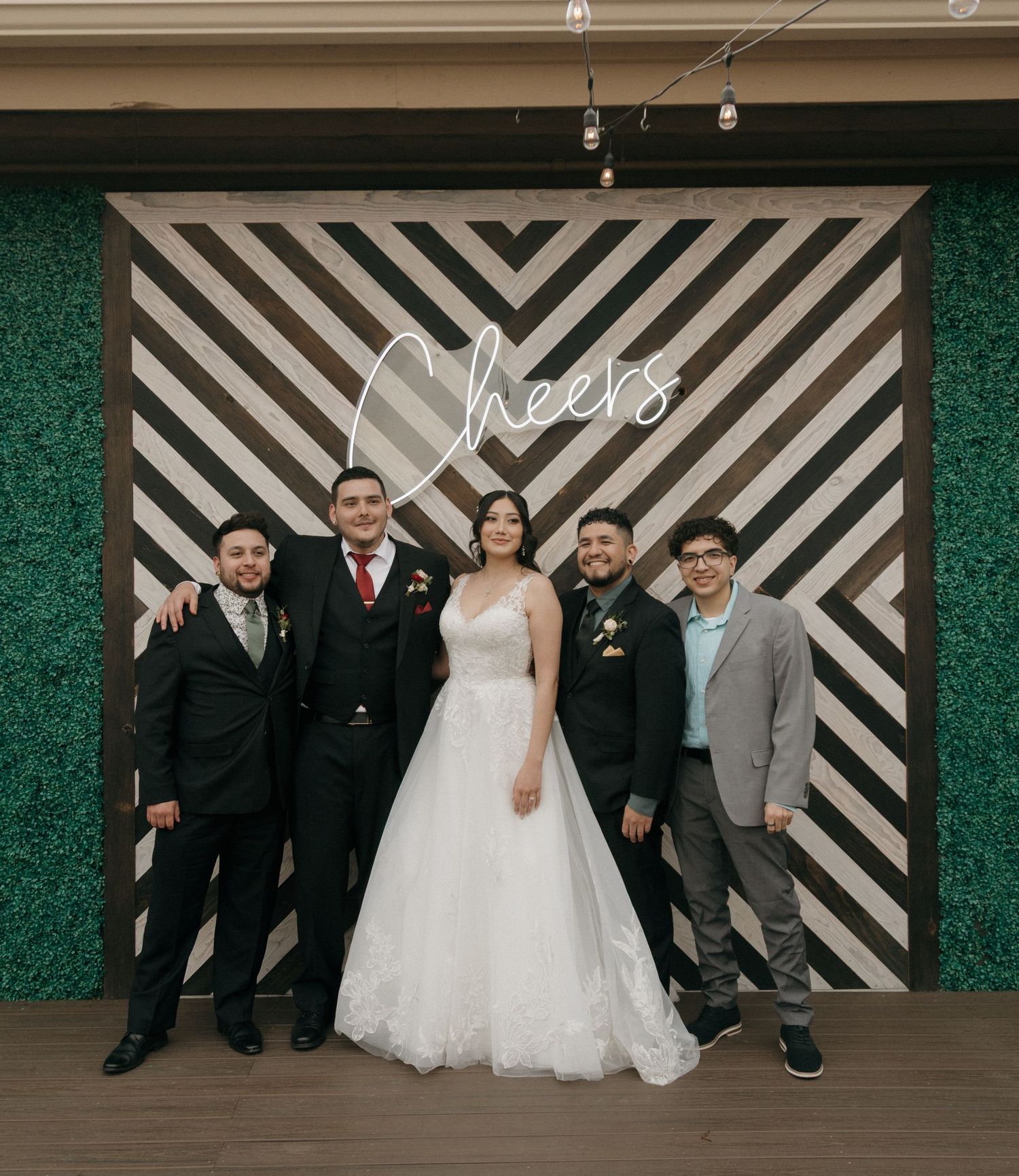 Bride and groom posing with three guests in front of a Cheers wedding photo backdrop.