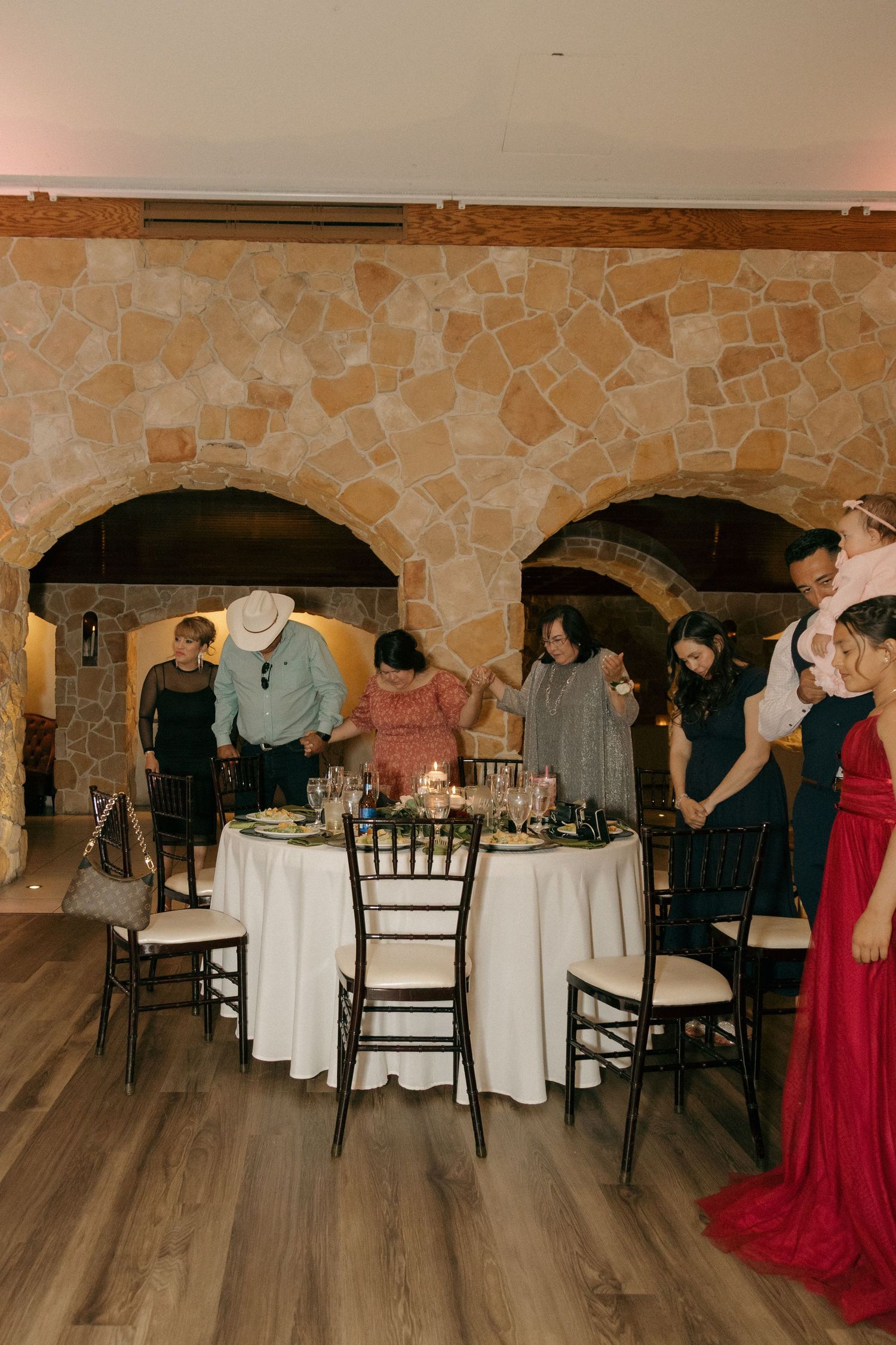 Wedding guests gather around a candlelit table in a rustic stone-walled reception venue.