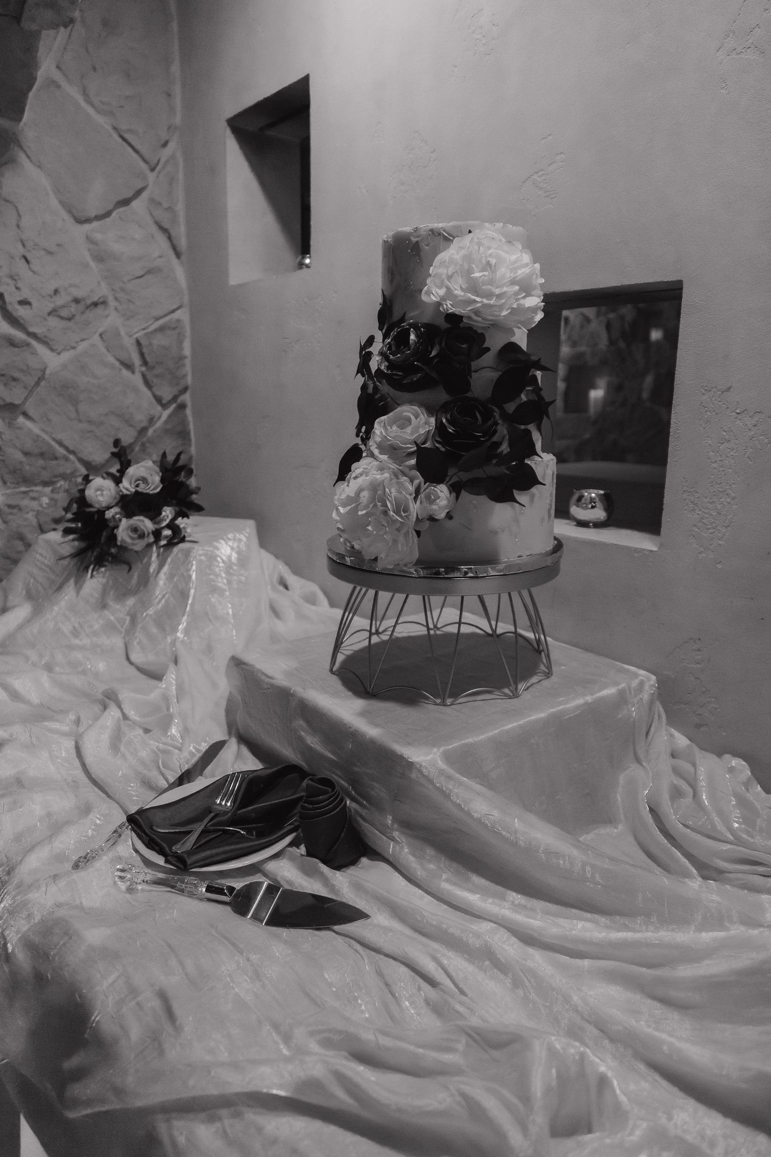 Elegant three-tier wedding cake with floral decorations displayed on a table in black and white.