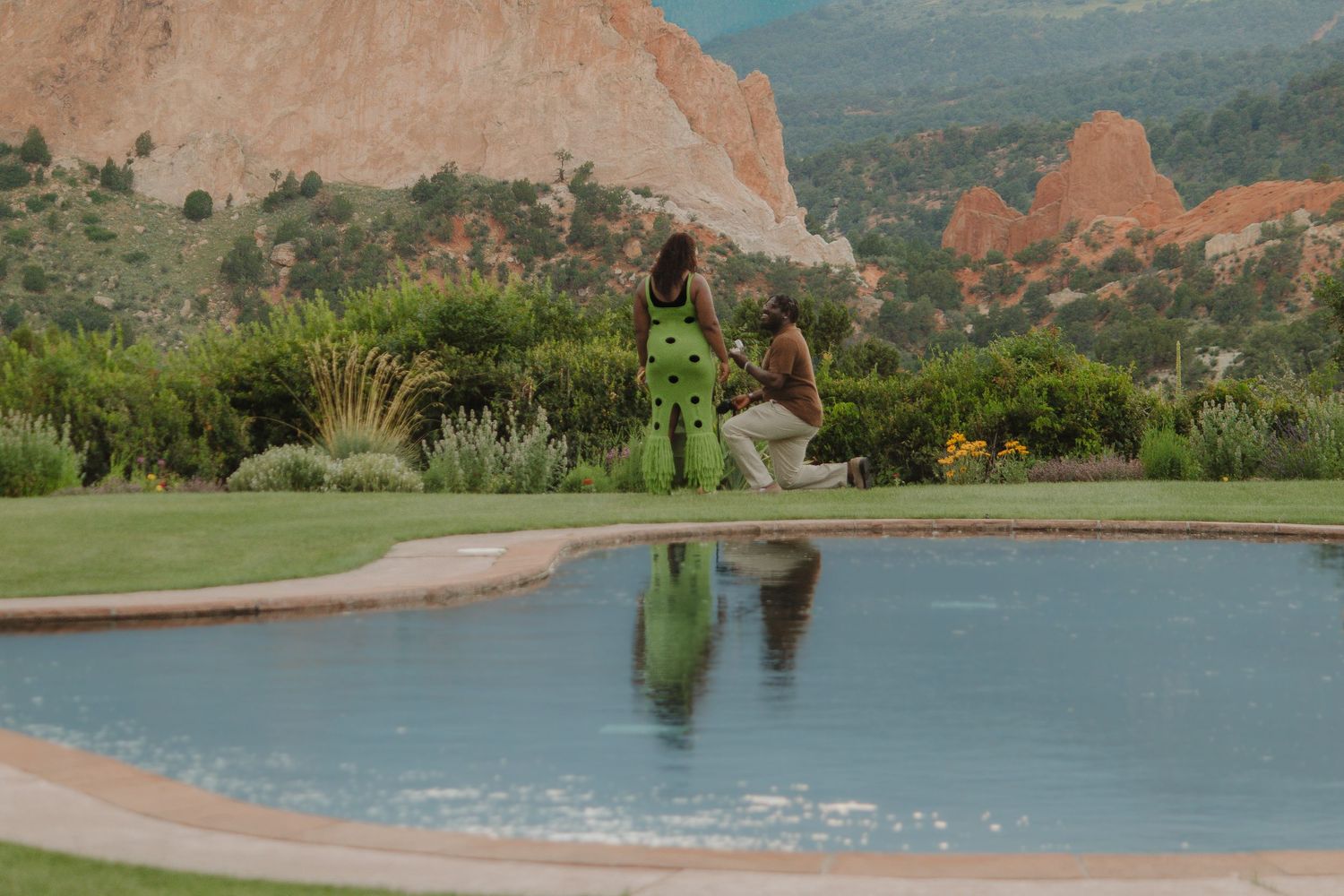 A silhouetted figure in green stands near a reflective pool with red rock formations in the background.