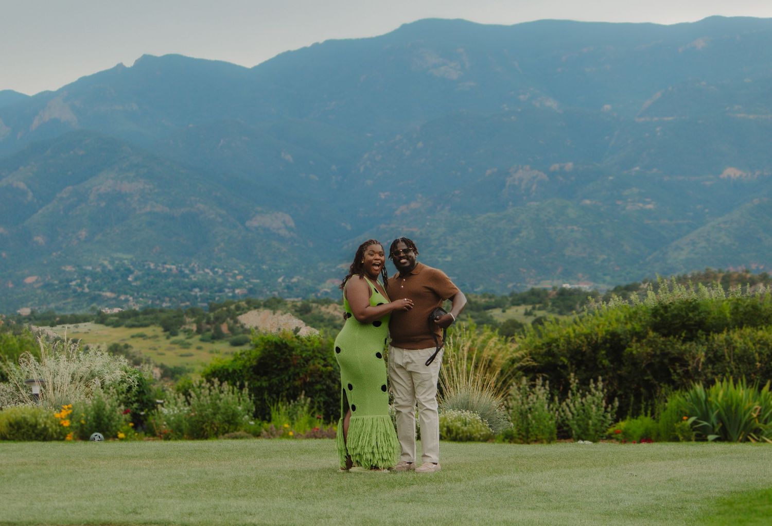 People walking along a scenic mountain path with rolling hills and lush greenery in the background.