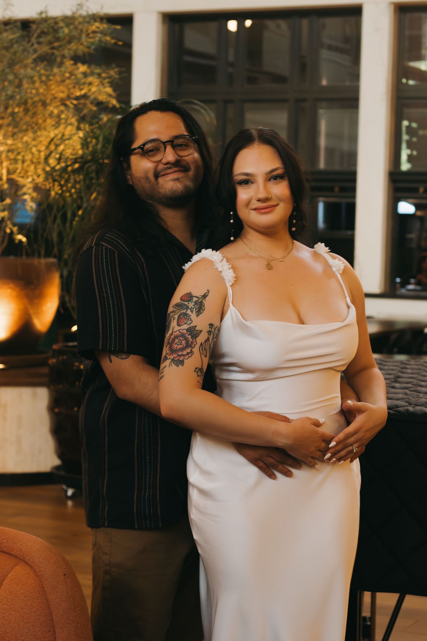 A couple poses together in formal attire at an elegant venue with warm ambient lighting.