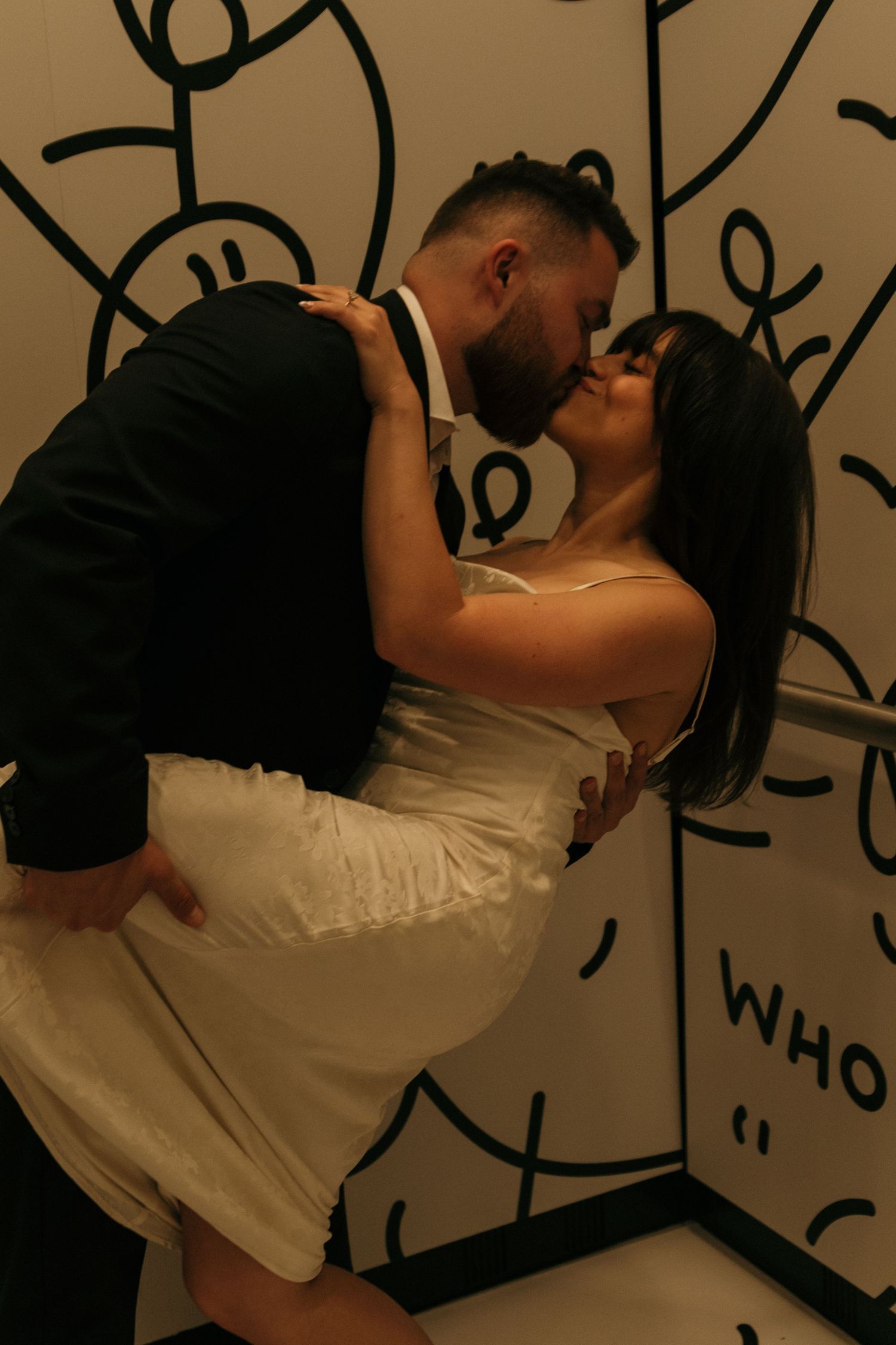 A couple shares a romantic moment against a wall with abstract artwork.