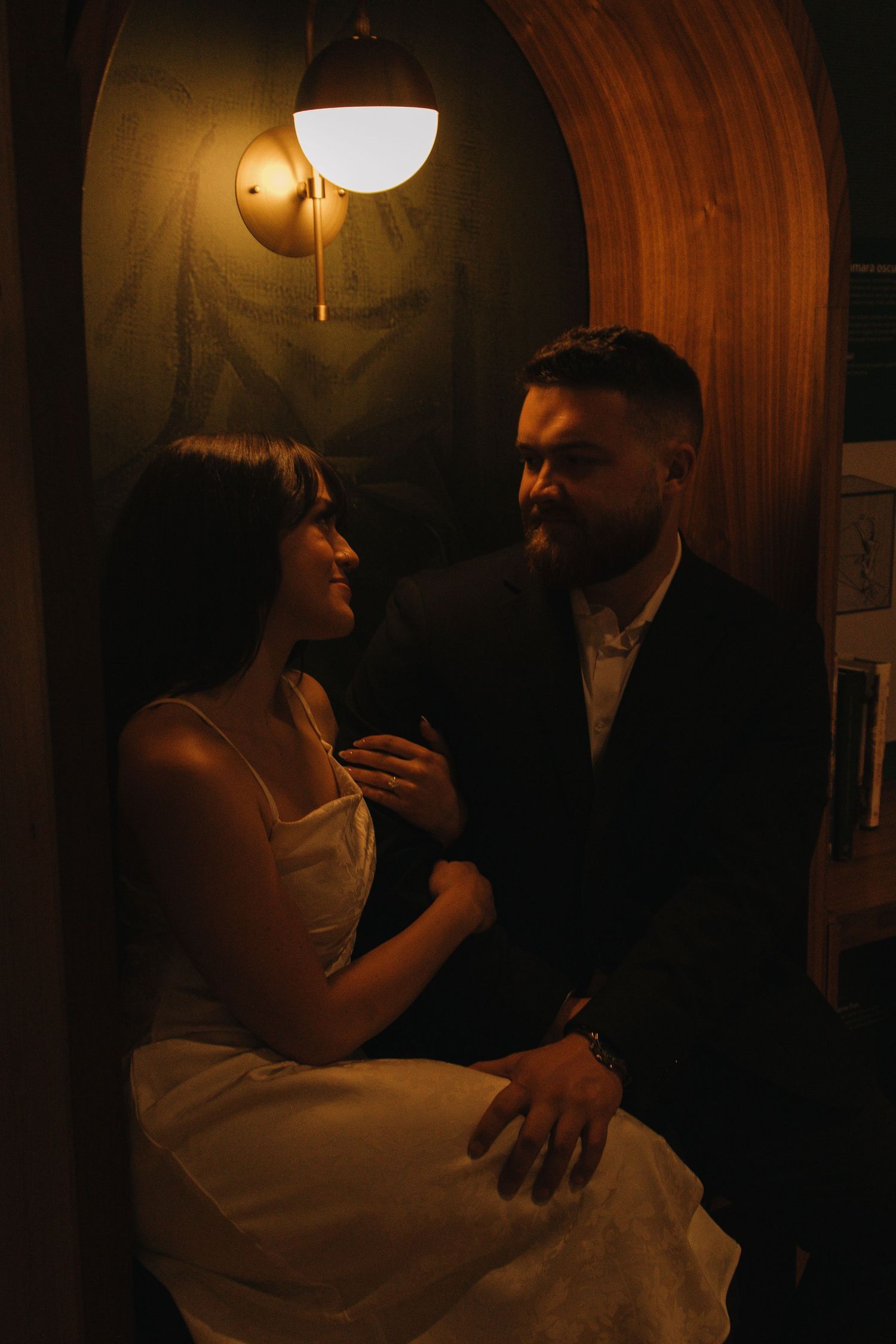 Intimate moment captured in dimly lit wood-paneled room with wall sconces.