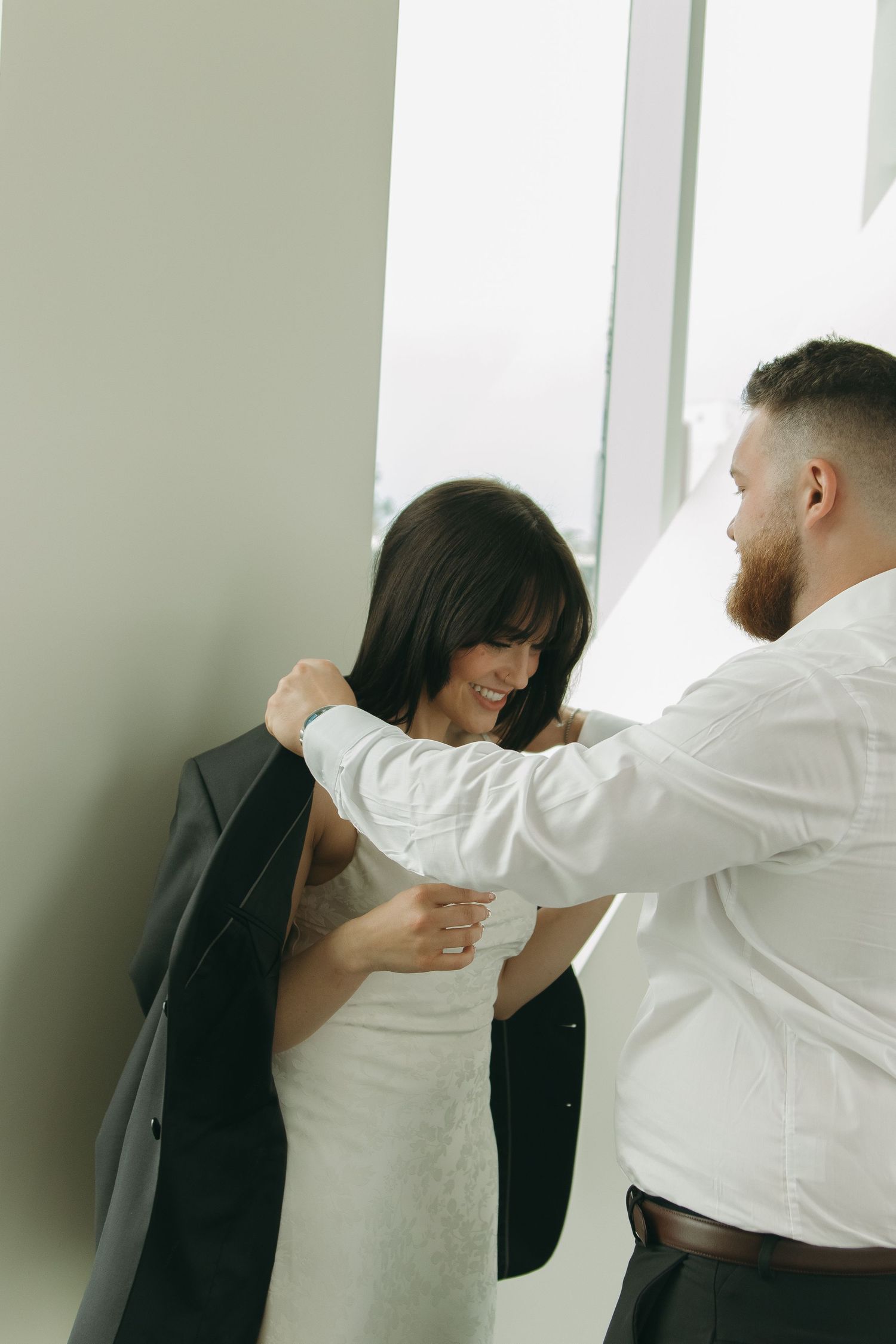 Candid moment of couple laughing while getting dressed in bright minimal room.