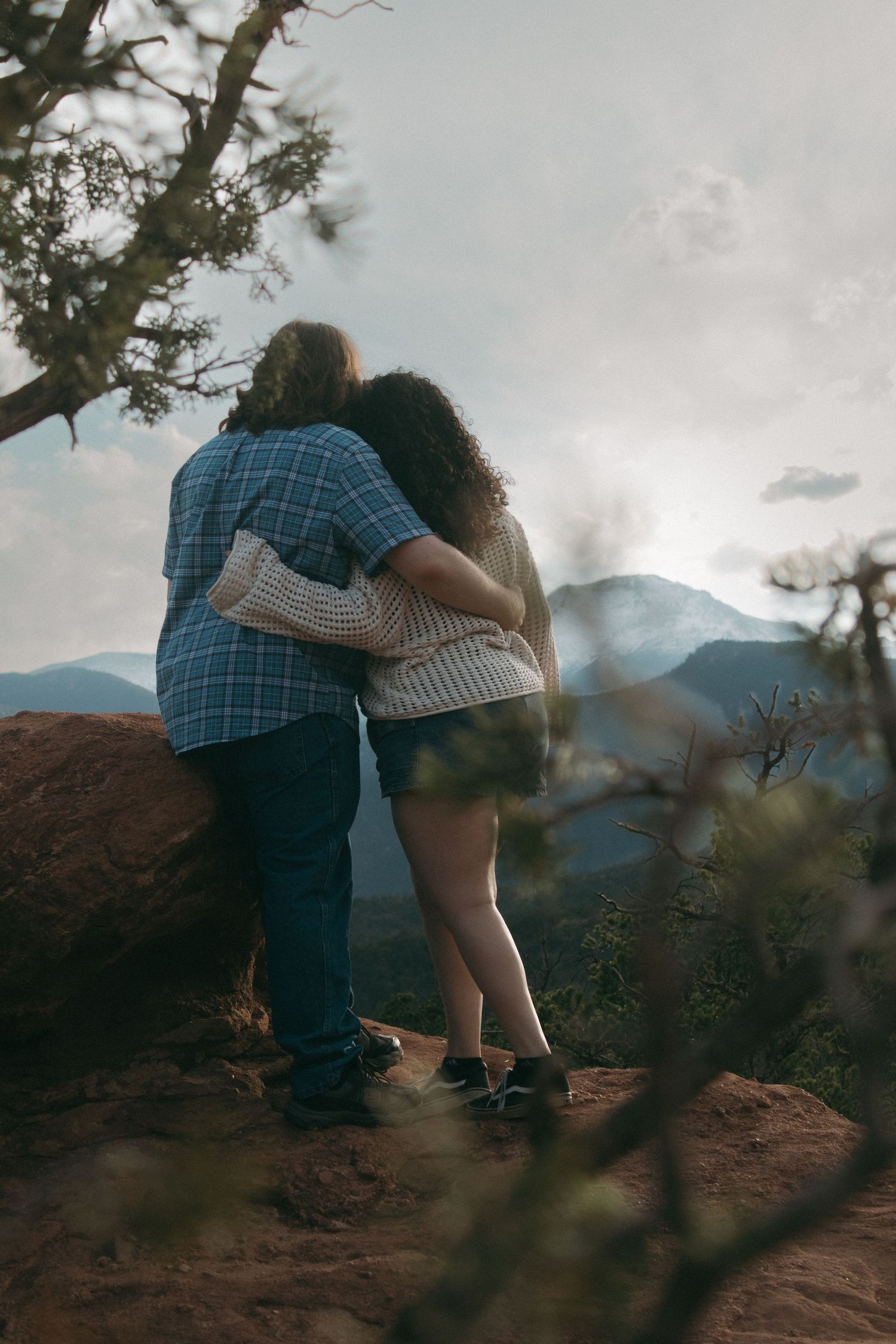 A couple embraces while standing on rocky terrain with mountains in the background.