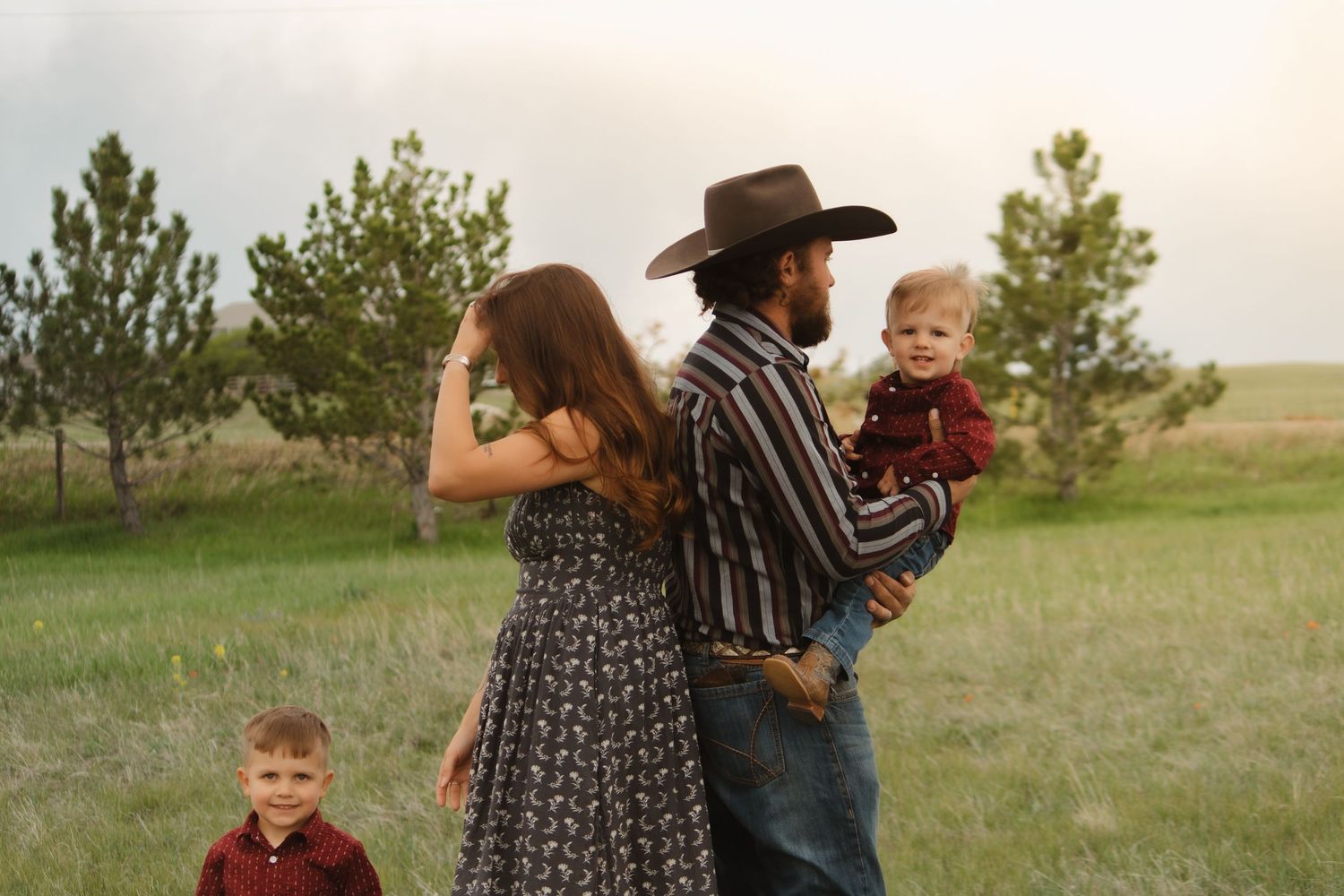 A family wearing coordinated outfits enjoys a casual outdoor photo session in a grassy field.