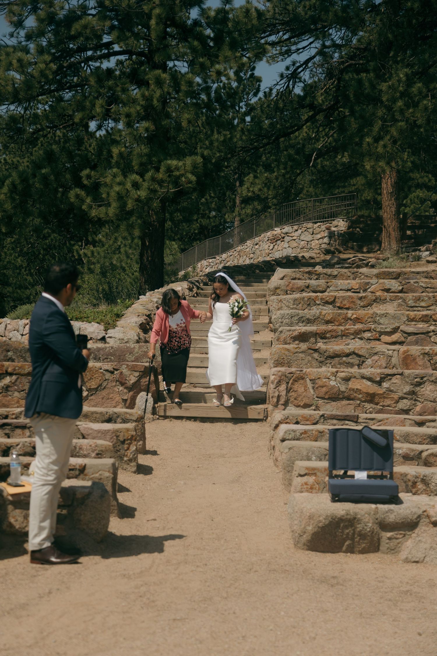 Bride in white gown and veil walks down stone steps at outdoor wedding venue.