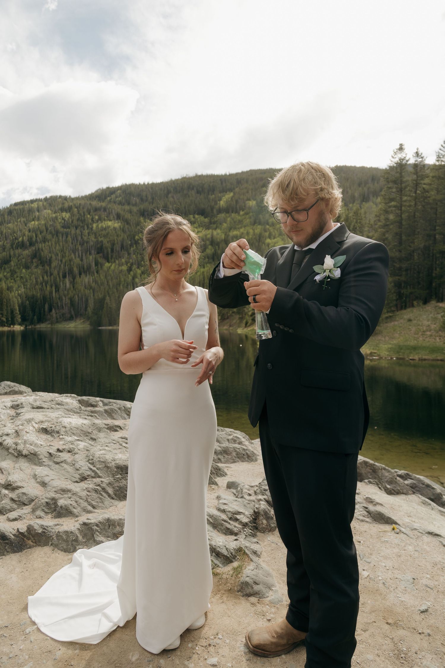 Bride and groom performing a sand ceremony by a mountain lake during their outdoor wedding.