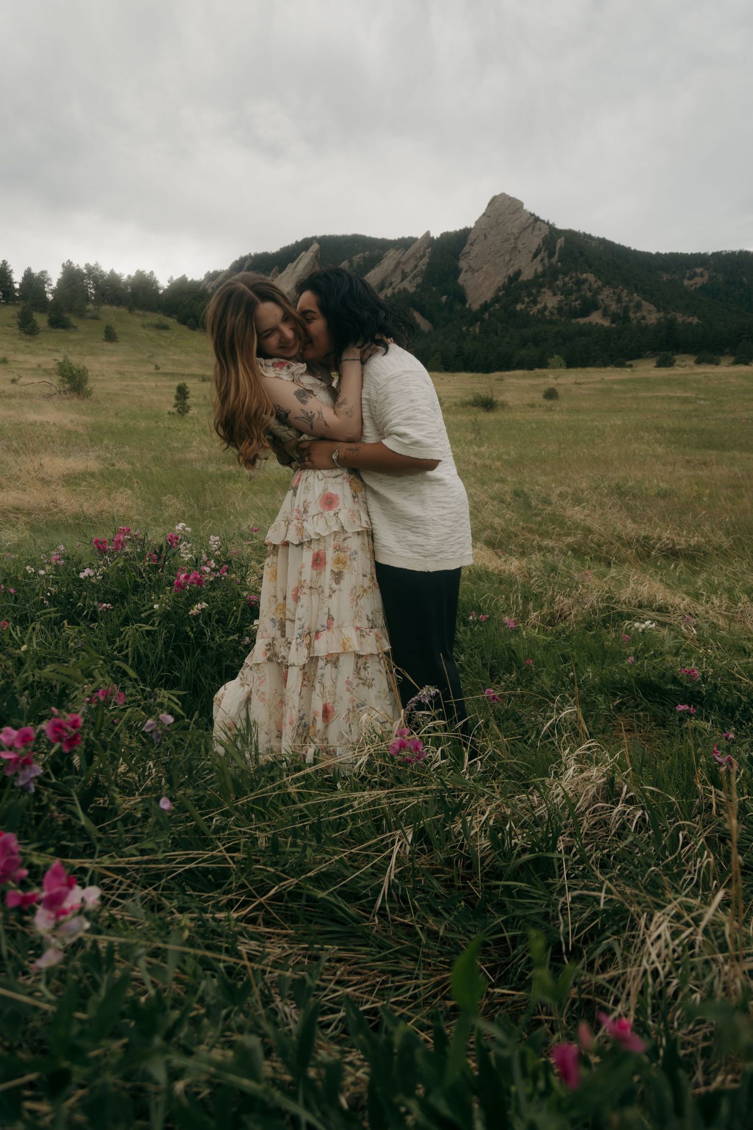 Couple embracing in a wildflower meadow with the Boulder Flatirons mountains in the background.