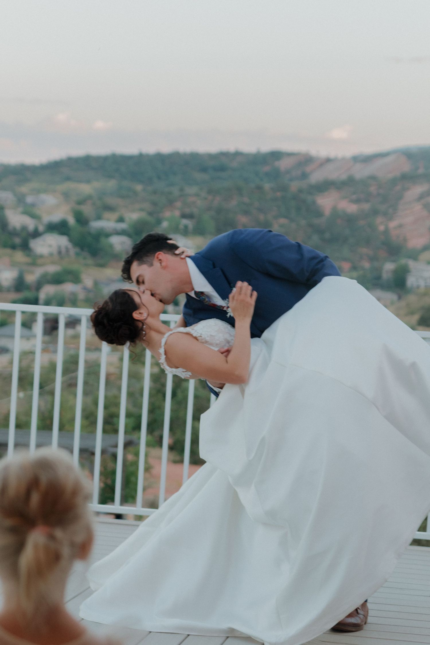 Dramatic dip kiss on terrace with mountain scenery in background.