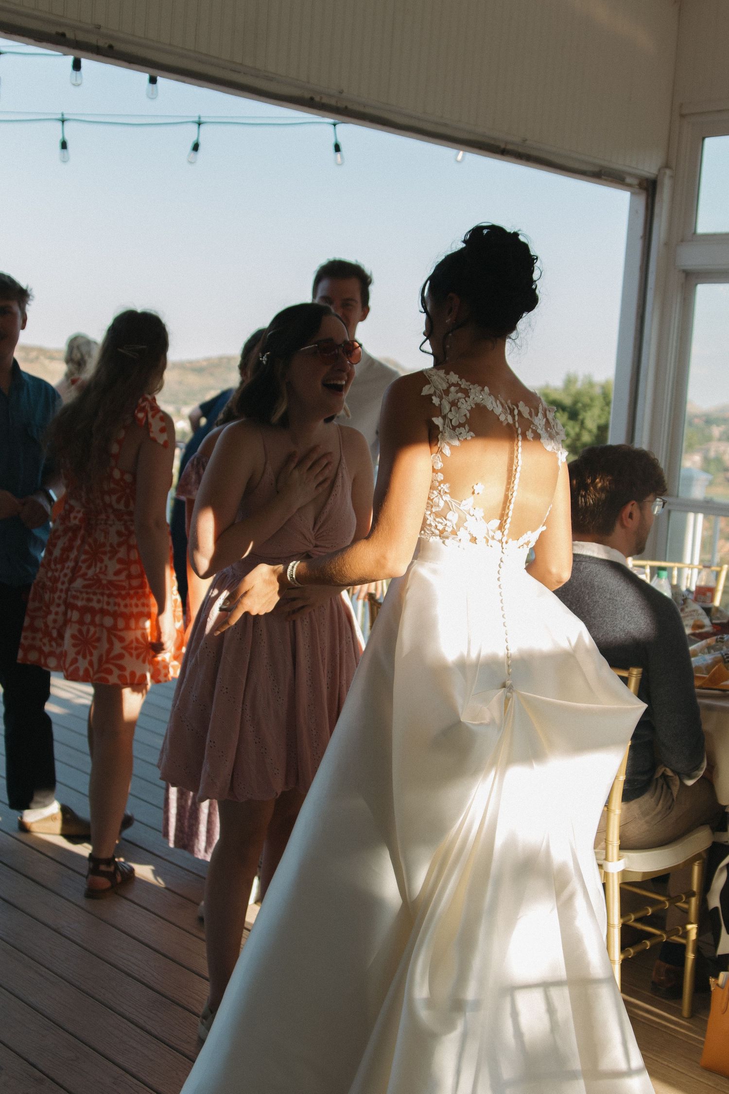 Wedding party celebrates on sunlit deck during sunset reception.